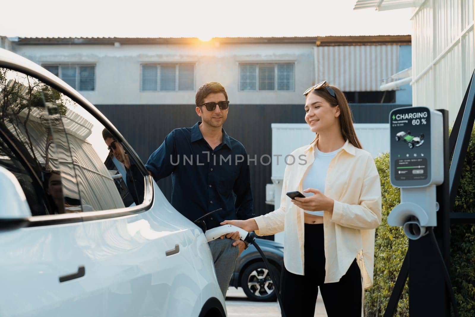 Eco-friendly conscious family couple recharging EV vehicle from home charging station. EV electric car technology utilized as alternative transportation for future sustainability. Expedient