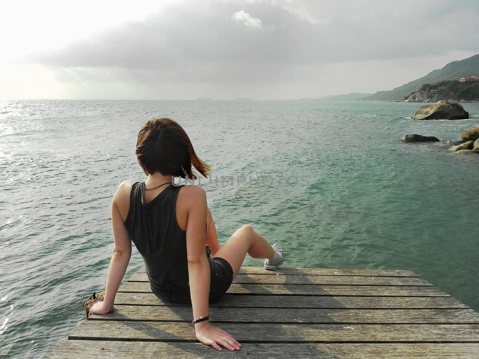 A girl sits on an open pier and looks at the sea