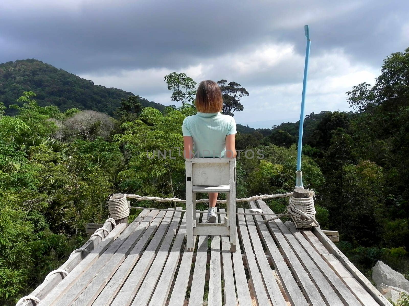 Woman hiker sitting alone on a wooden chair overlooking the green mountains. View point on Koh Phangan