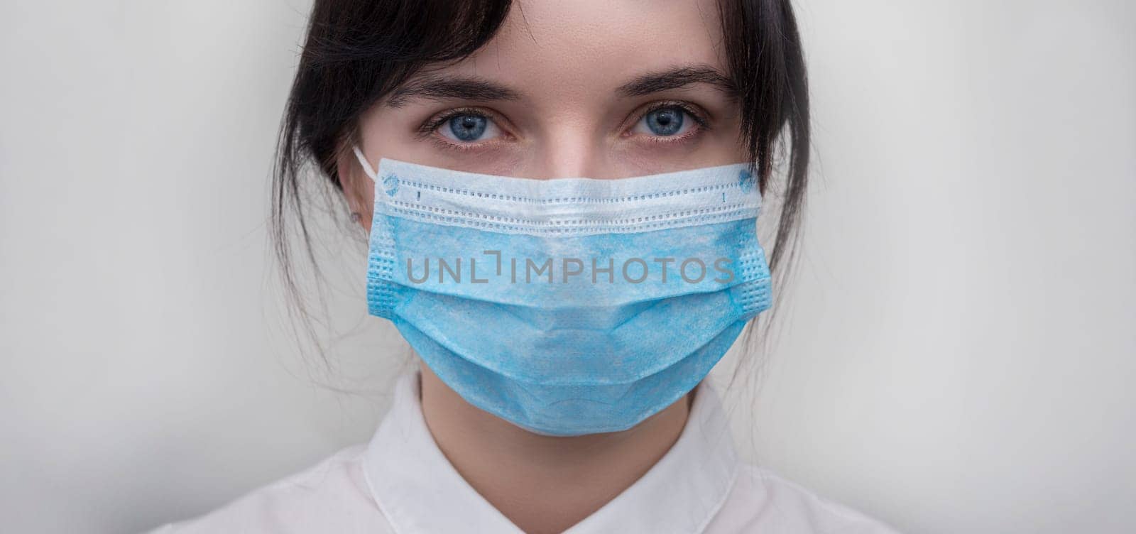 Portrait of a young European woman in a protective disposable medical mask. Concept of caronavirus Cavid 19 and human quarantine. Girl in a mask on a white wall. Masked medical worker