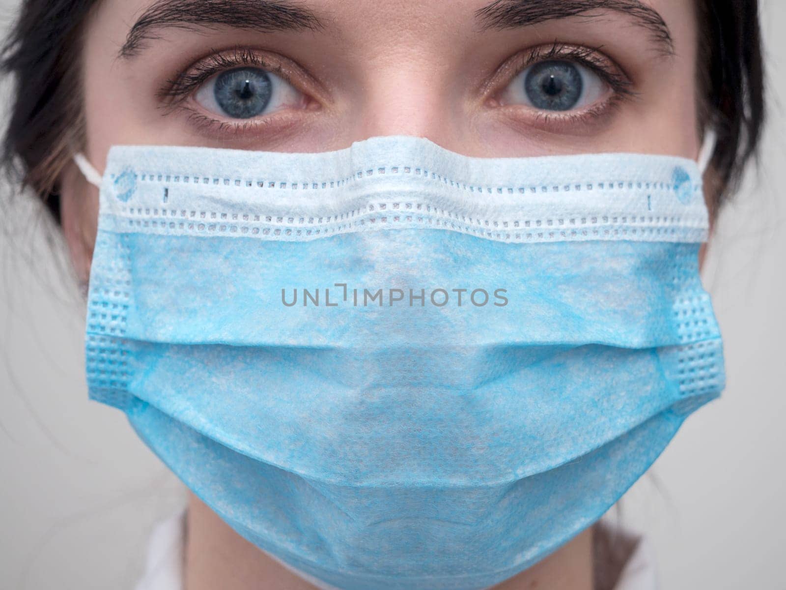 Portrait of a young European woman in a protective disposable medical mask. Concept of caronavirus Cavid 19 and human quarantine. Girl in a mask on a white wall. Masked medical worker