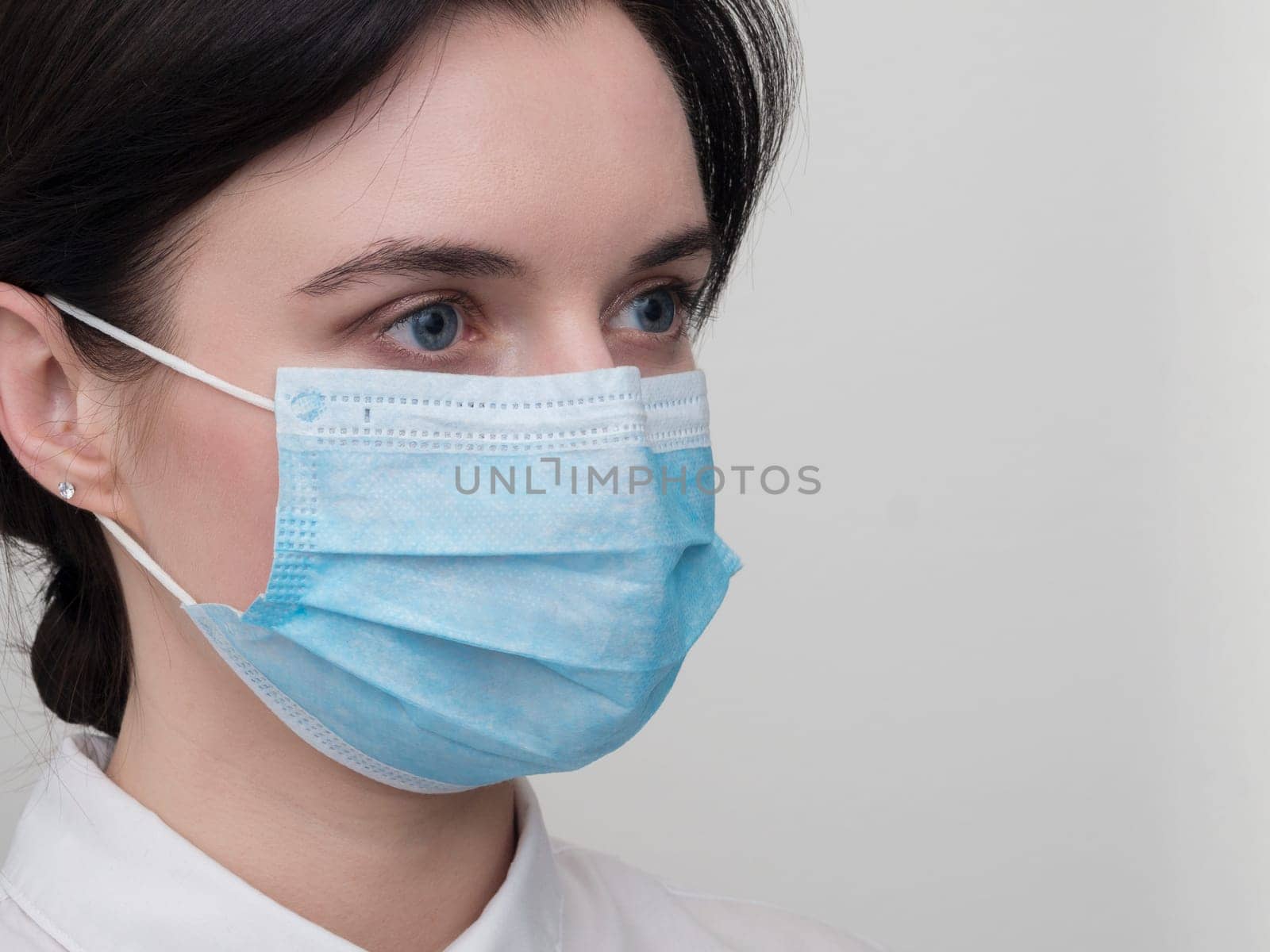 Portrait of a young European woman in a protective disposable medical mask. Concept of caronavirus Cavid 19 and human quarantine. Girl in a mask on a white wall. Masked medical worker