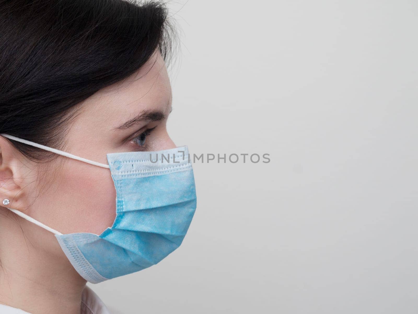 Portrait of a young European woman in a protective disposable medical mask. Concept of caronavirus Cavid 19 and human quarantine. Girl in a mask on a white wall. Masked medical worker