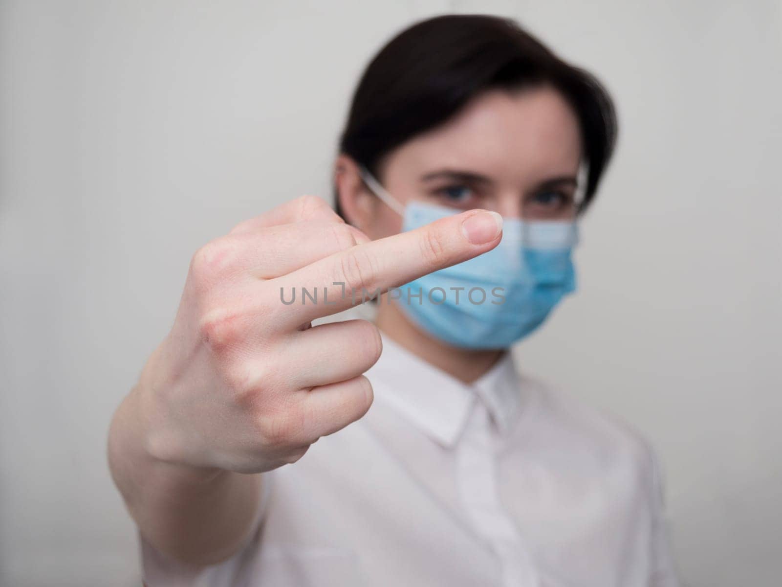 Woman with a medical mask and gloves shows by hand the symbol of the fuck off. Coronavirus concept. Fuck you corona