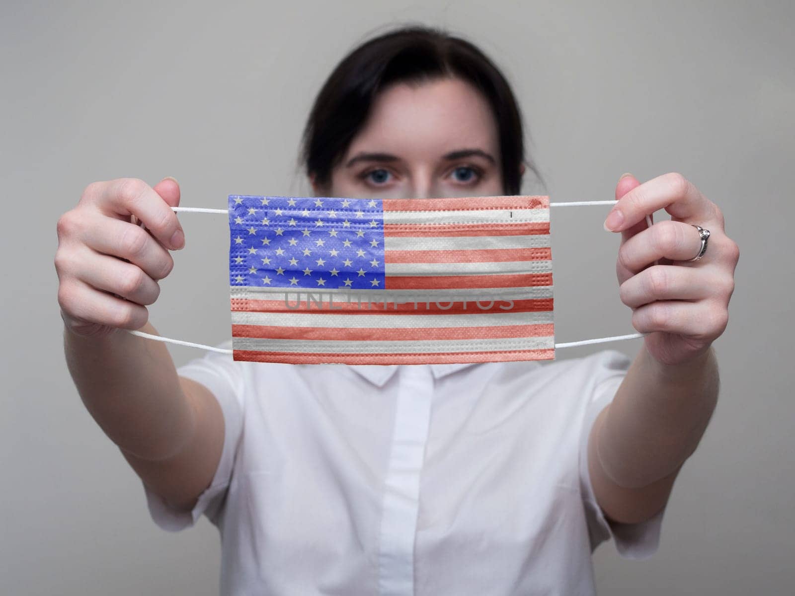 A woman holds out a Medical mask with the image of the flag of the United States of America (USA) in her hands. Coronavirus COVID-19