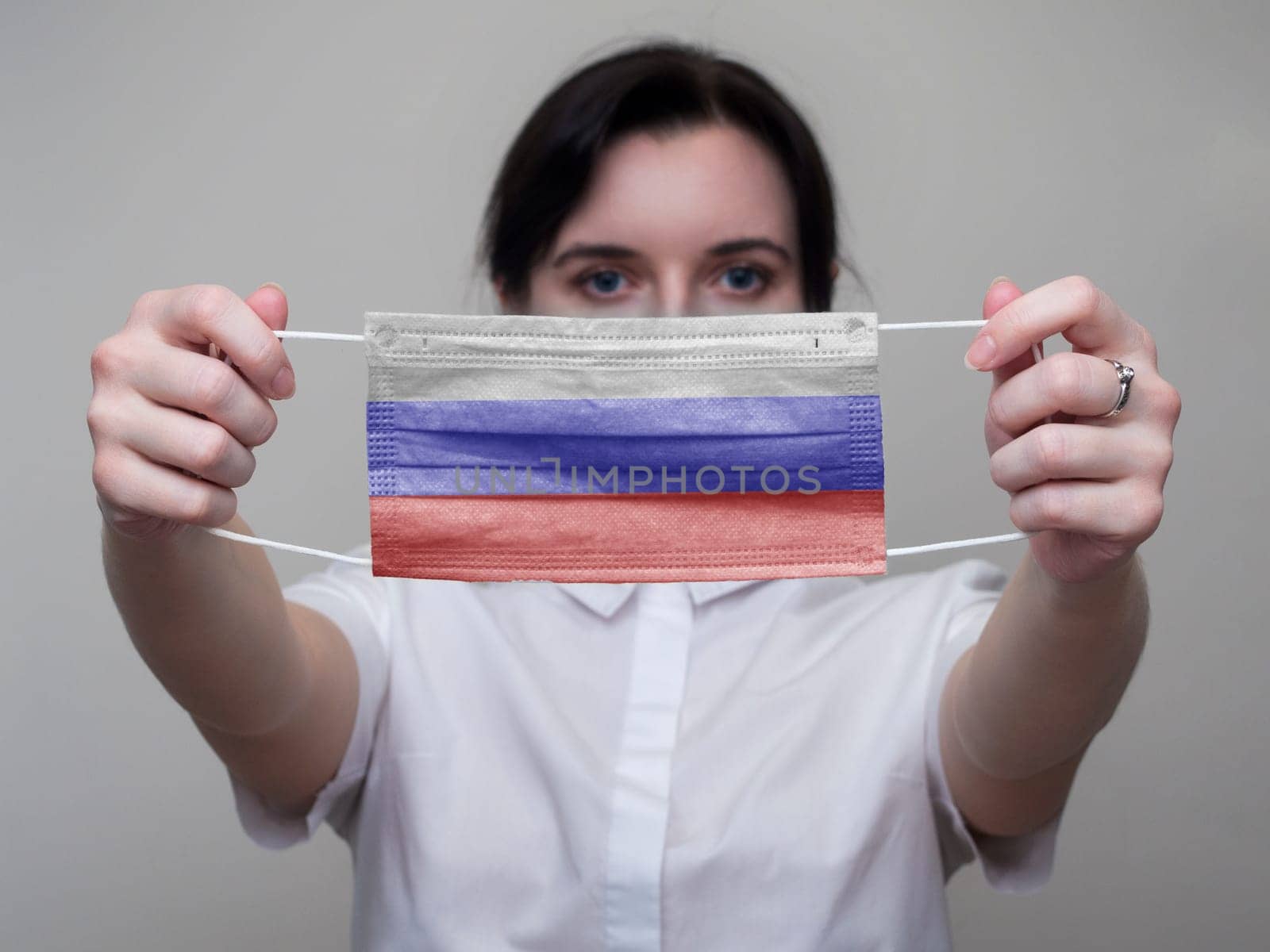 Woman holds out a medical mask with the image of the flag of Russia in her hands. Coronavirus COVID-19