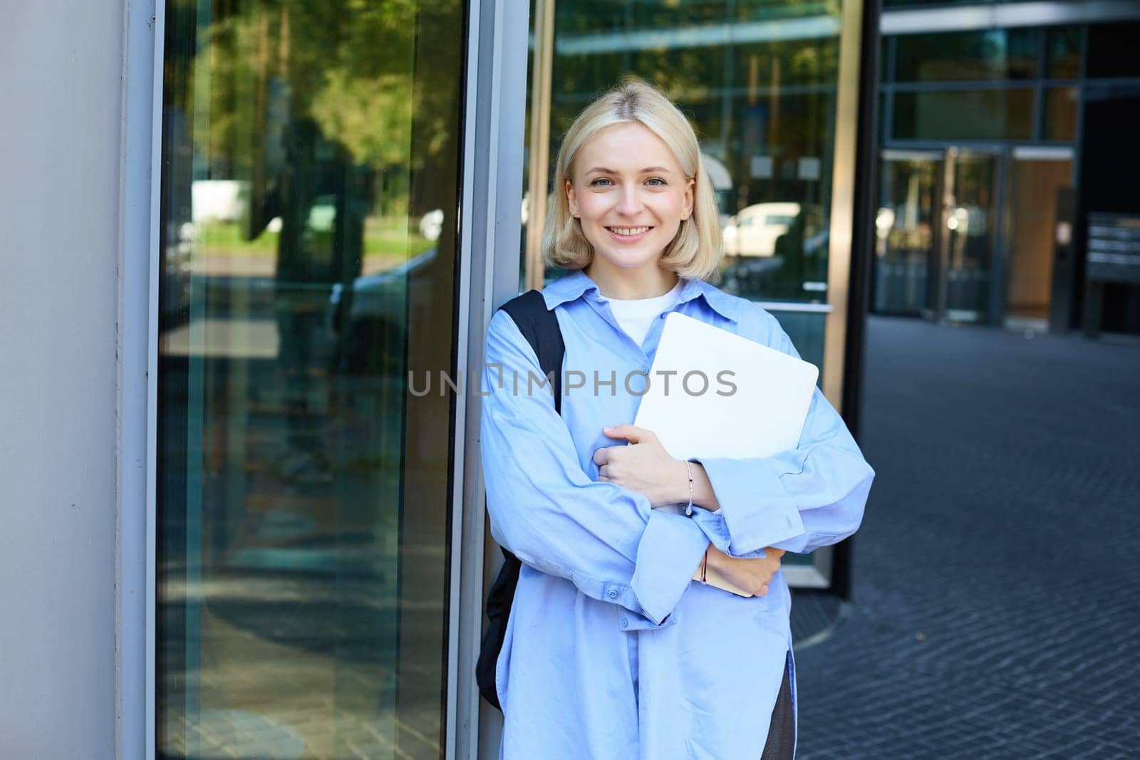 Image of young college girl, young woman with laptop, posing near university building, standing on street, smiling, concept of education and people by Benzoix