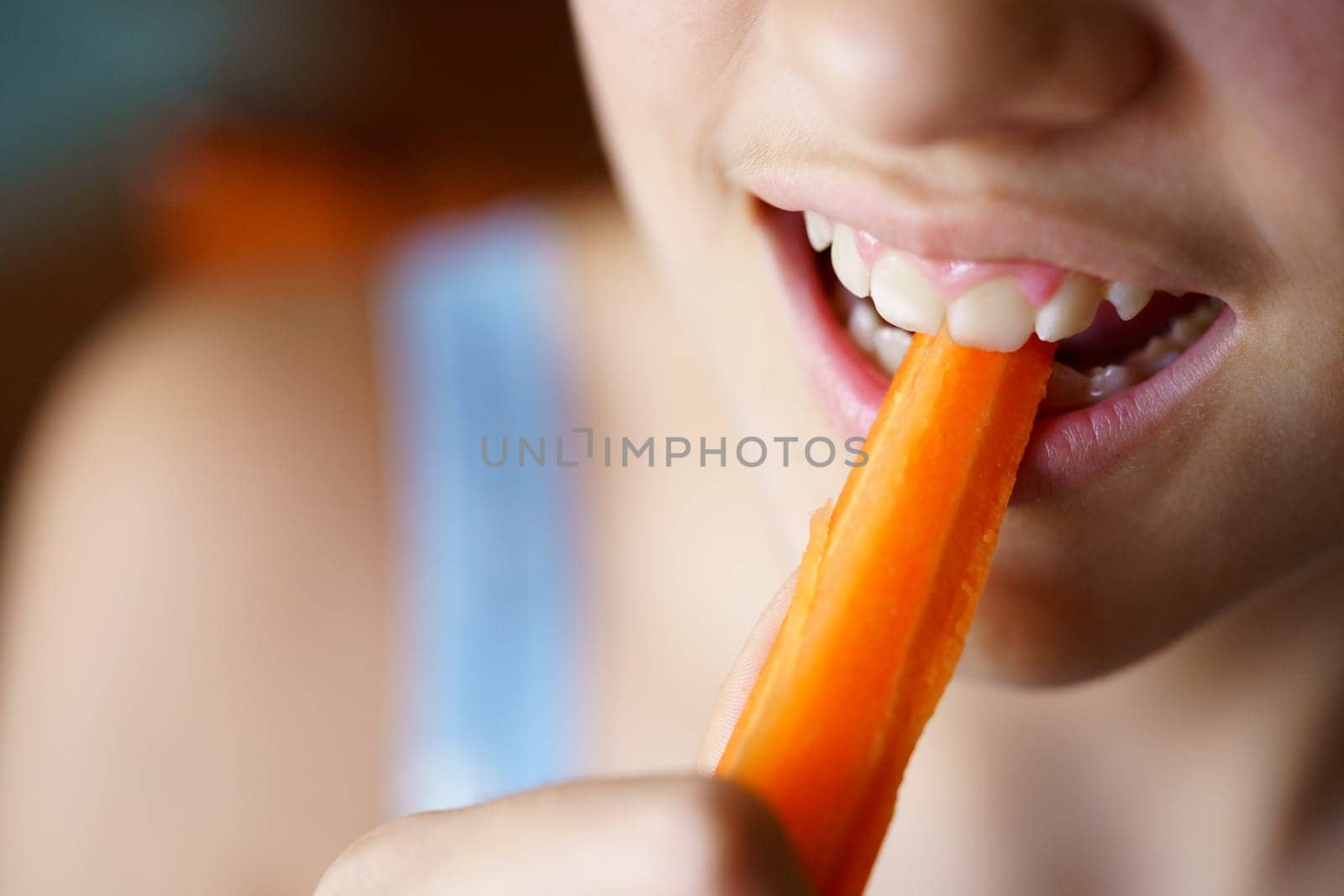High angle closeup of crop anonymous teenage girl biting fresh healthy carrot slice at home