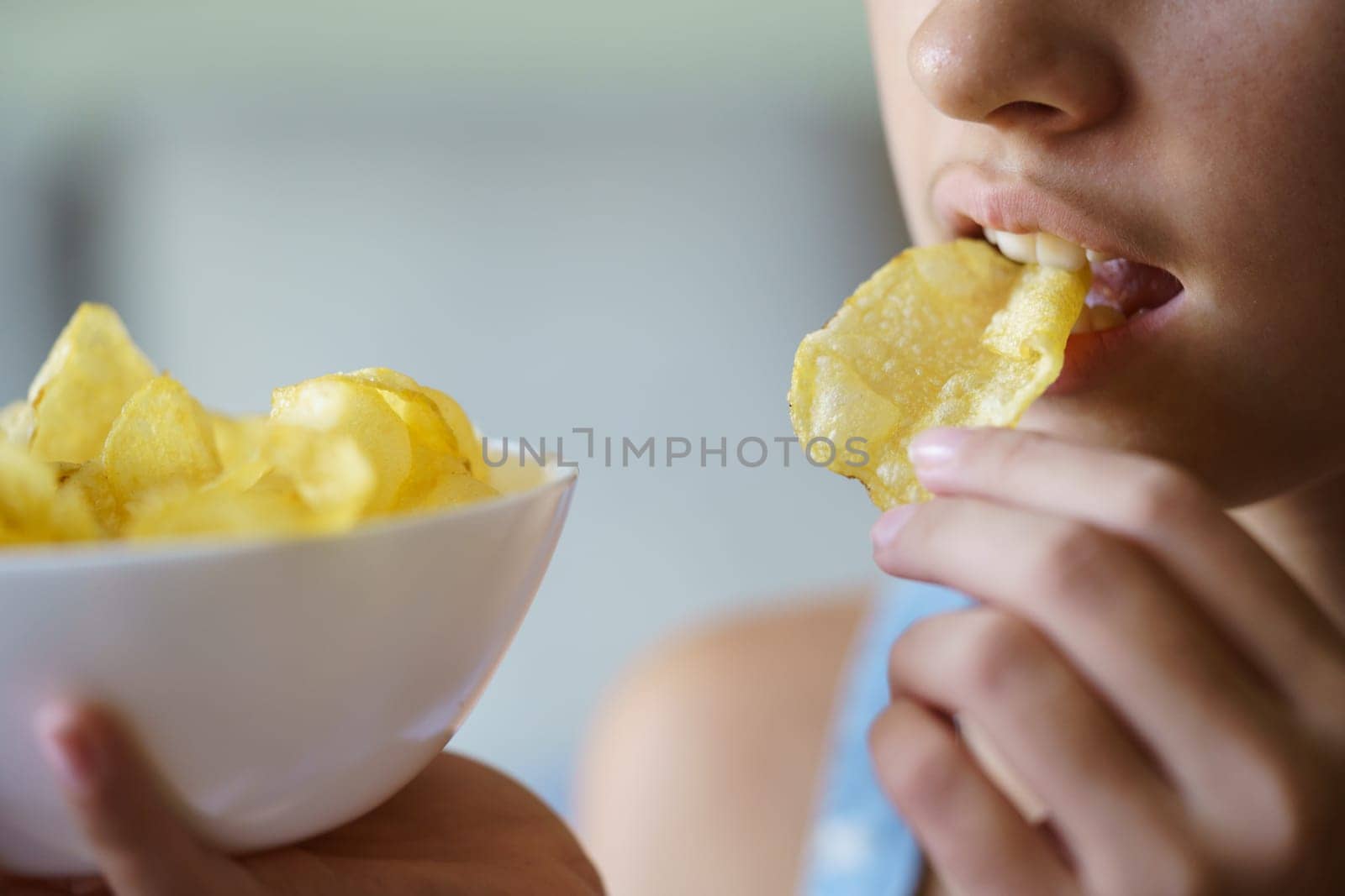 Crop teenage girl eating crispy potato chip while holding bowl by javiindy