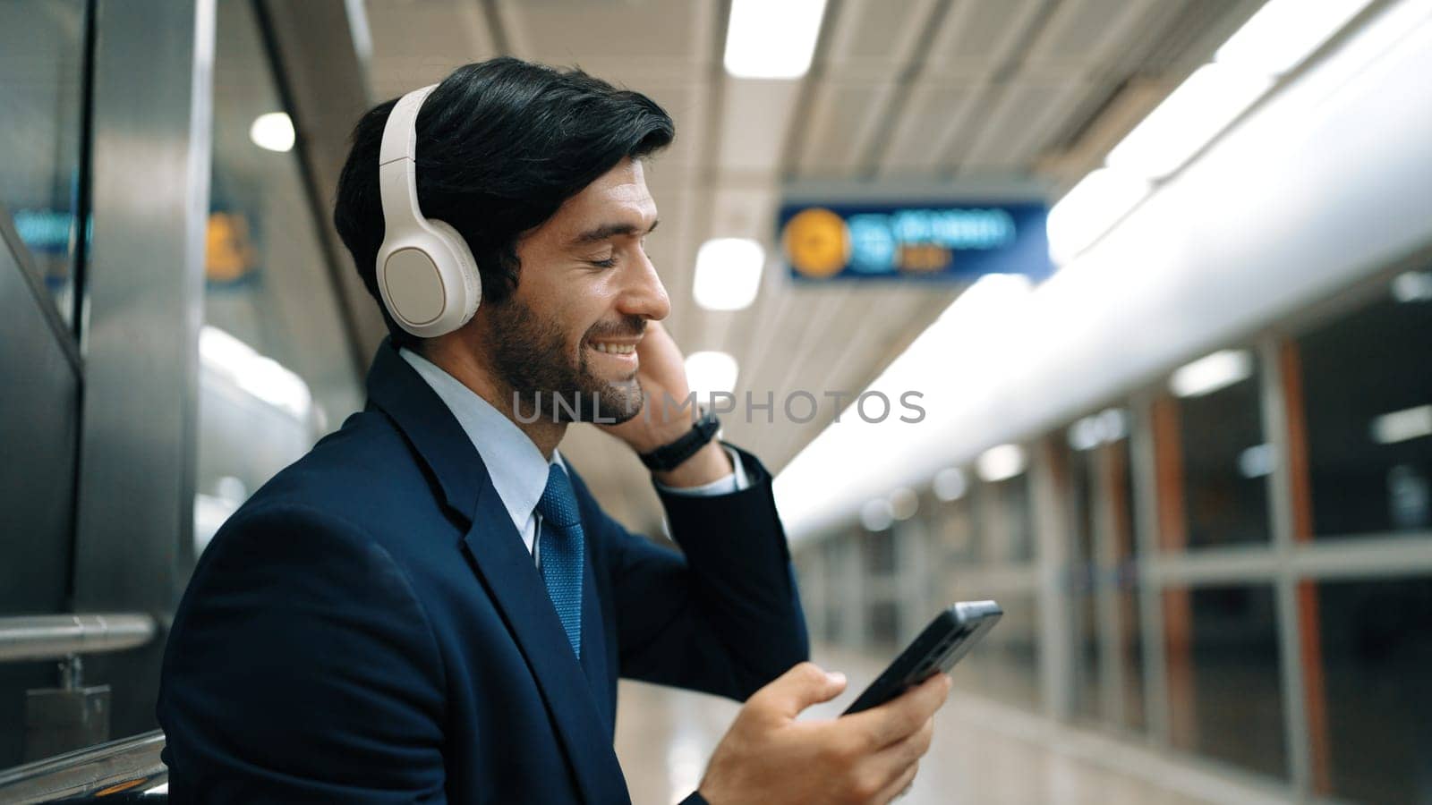 Smart business man listen music while waiting train at train station. Exultant. by biancoblue