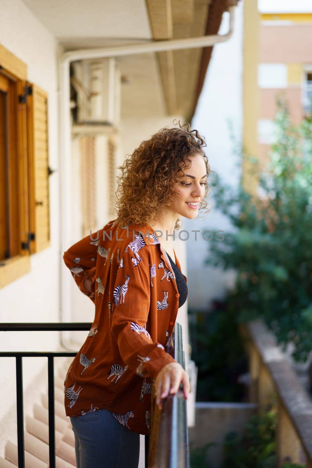 Smiling young woman standing on balcony in modern apartment by javiindy