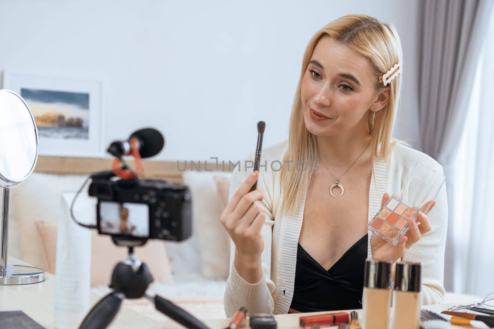 Young woman making beauty and cosmetic tutorial video content for social media. Beauty blogger smiles to camera while showing how to beauty care to audience or followers. Blithe