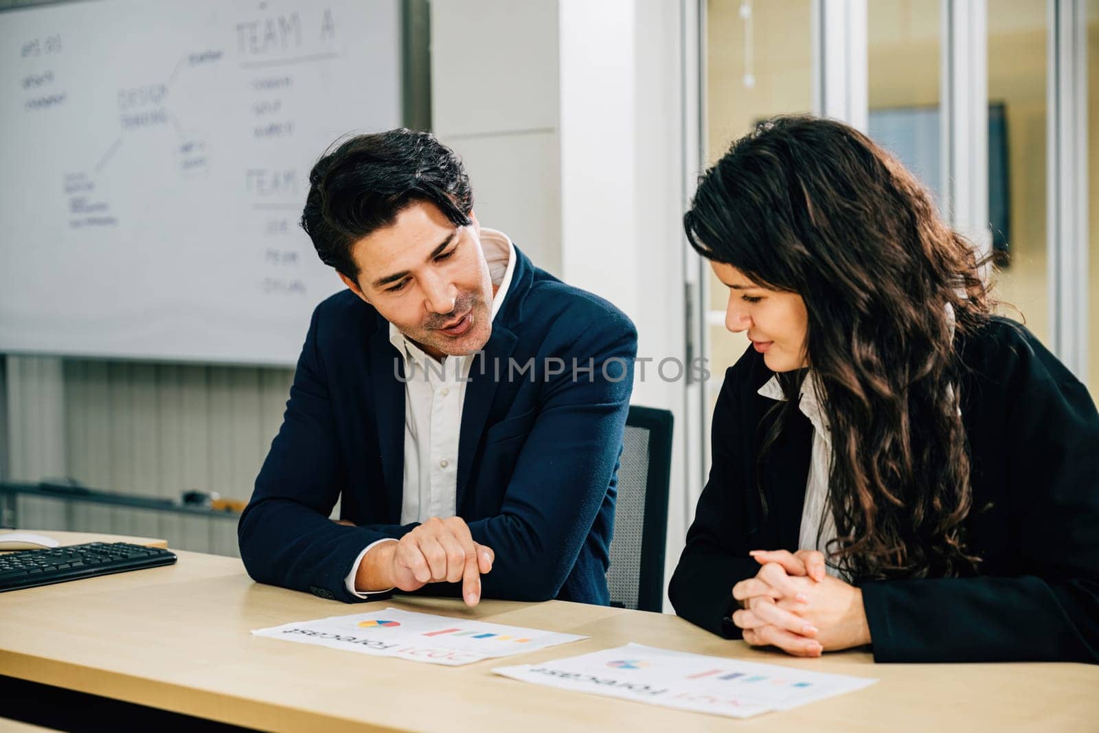 A pair of business partners meet in an office, brainstorming and discussing business strategy. They collaborate on paperwork, analyze graphs, and focus on financial success. teamwork by Sorapop