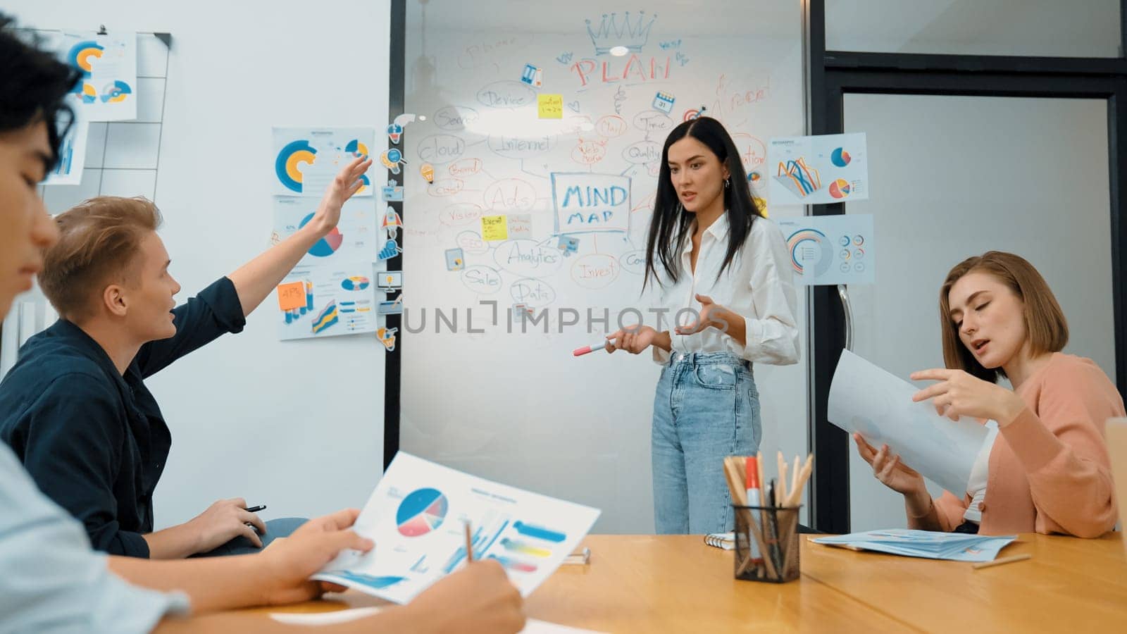 Closeup of young handsome caucasian raising hand and asking questions while young beautiful leader present business plan by using mind map and colorful graph between business meeting. Immaculate.