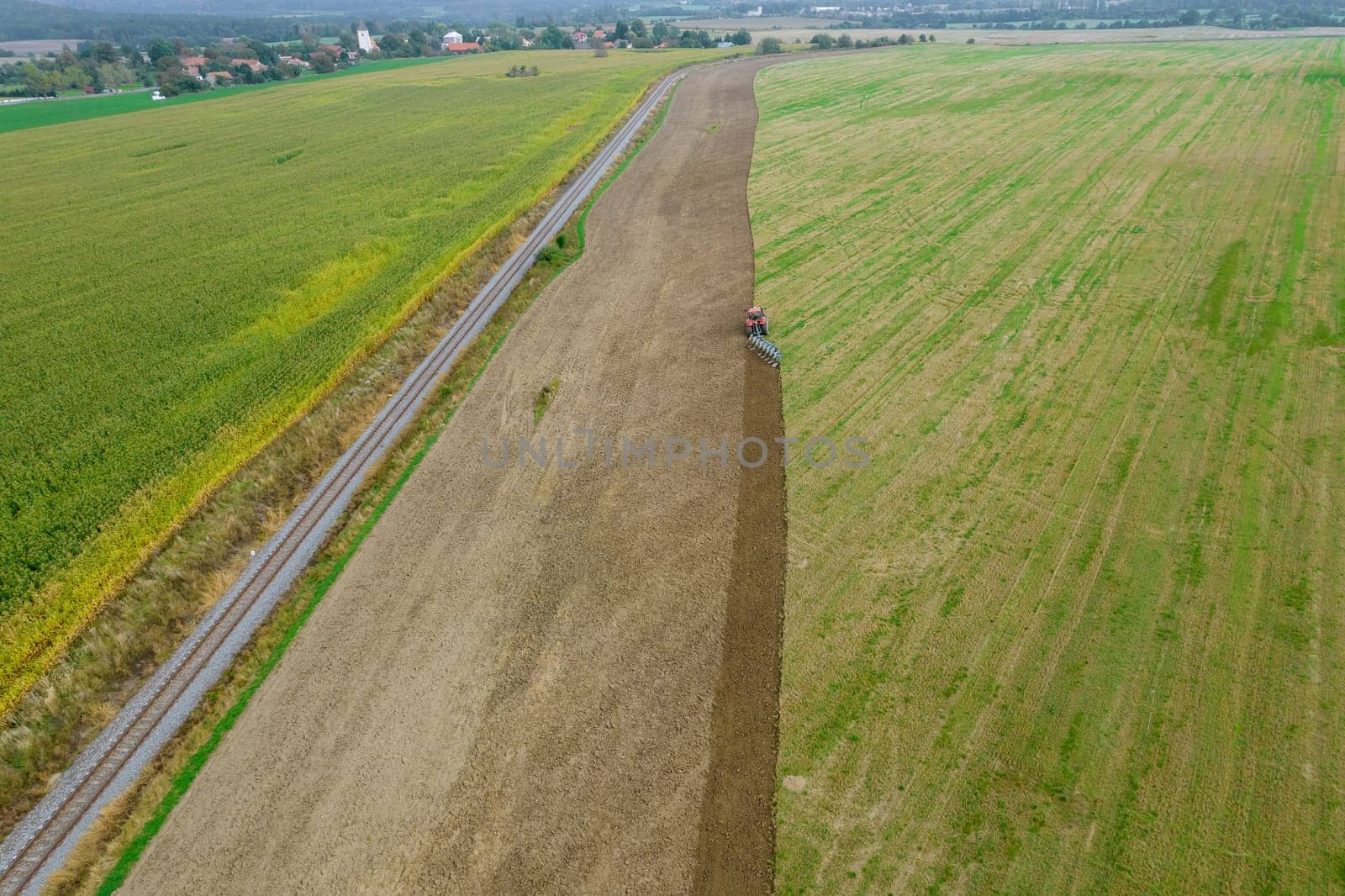 A tractor plows a field sown with green manure near a railway in a hilly area. Season of work in the farmer's field.