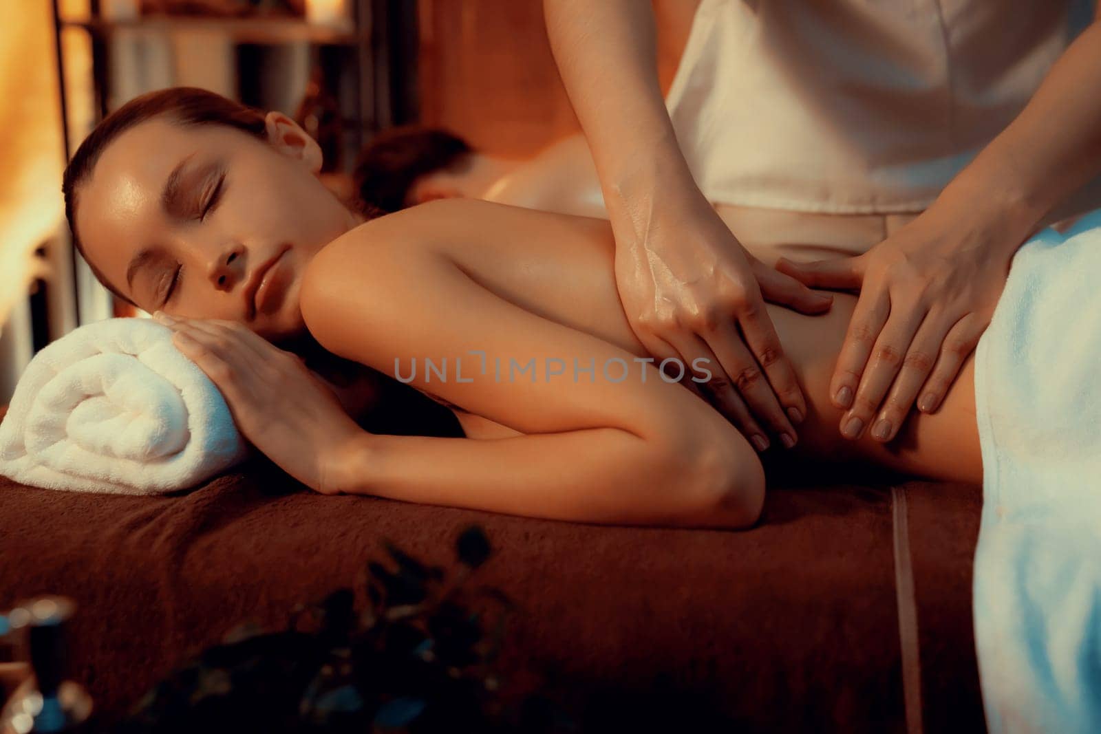 Caucasian couple customer enjoying relaxing anti-stress spa massage and pampering with beauty skin recreation leisure in warm candle lighting ambient salon spa at luxury resort or hotel. Quiescent