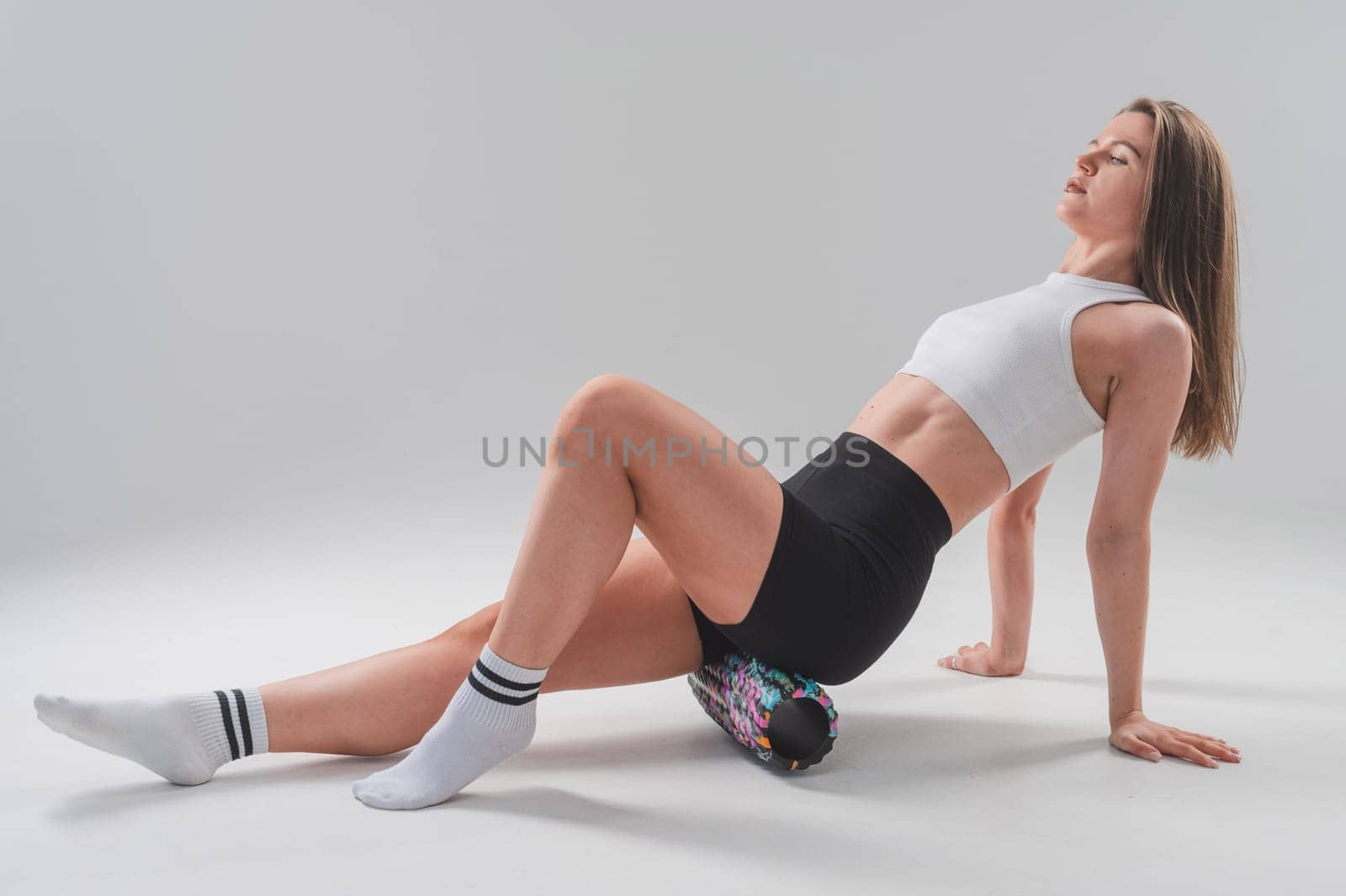 Caucasian woman doing roller exercise for myofascial release on white background. Self-massage of thighs. by mrwed54