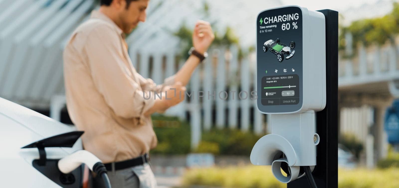 Young man put EV charger to recharge electric car's battery from charging station in city commercial parking lot. Rechargeable EV car for sustainable environmental friendly urban travel. Expedient