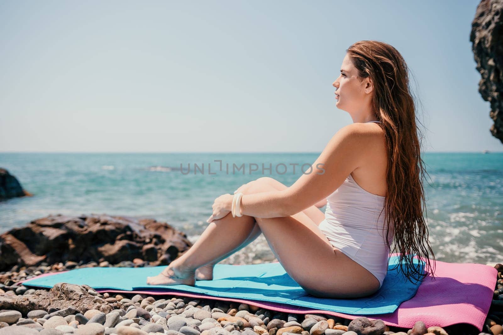 Woman sea fitness. Happy woman with long hair, fitness instructor in white bikini doing stretching and pilates on yoga mat near the sea. Female fitness yoga routine concept. Healthy lifestyle. by panophotograph