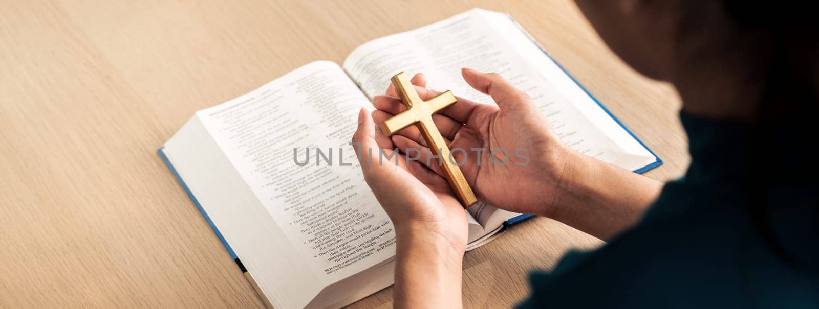 Female god believer holding wooden cross on opened holy bible book at light wooden church table. Top view. Concept of hope, religion, faith, christianity and god blessing. Warm background. Burgeoning.