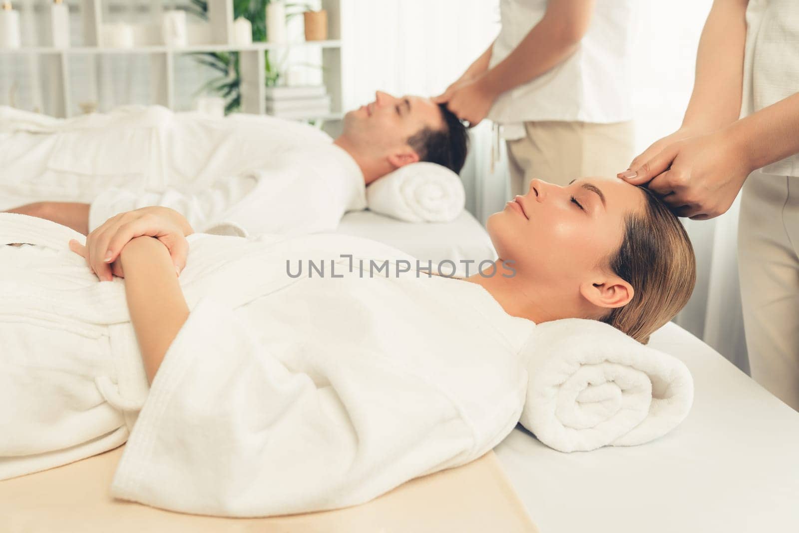 Caucasian couple enjoying relaxing anti-stress head massage and pampering facial beauty skin recreation leisure in dayspa modern light ambient at luxury resort or hotel spa salon. Quiescent