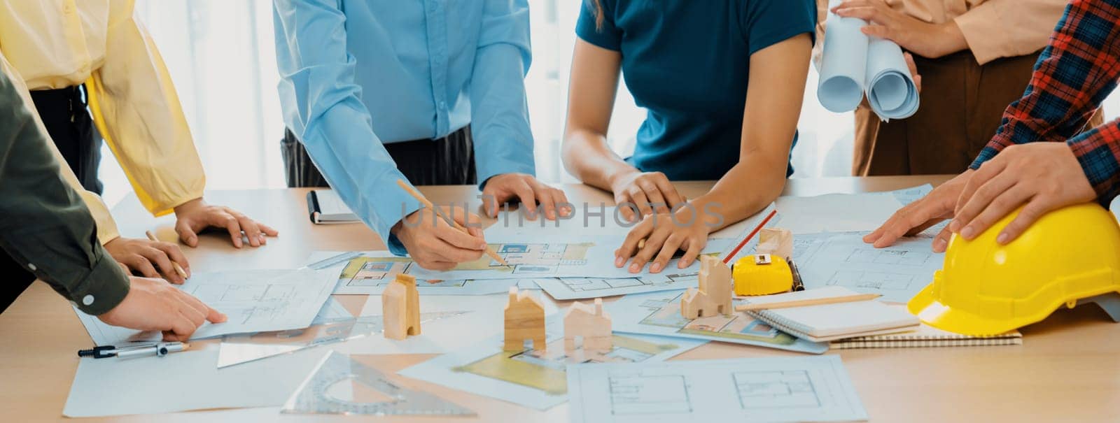 Professional architect engineer team discussion about architectural project on meeting table with wooden block and blueprint scatter around. Design and cooperate concept. Closeup. Delineation.