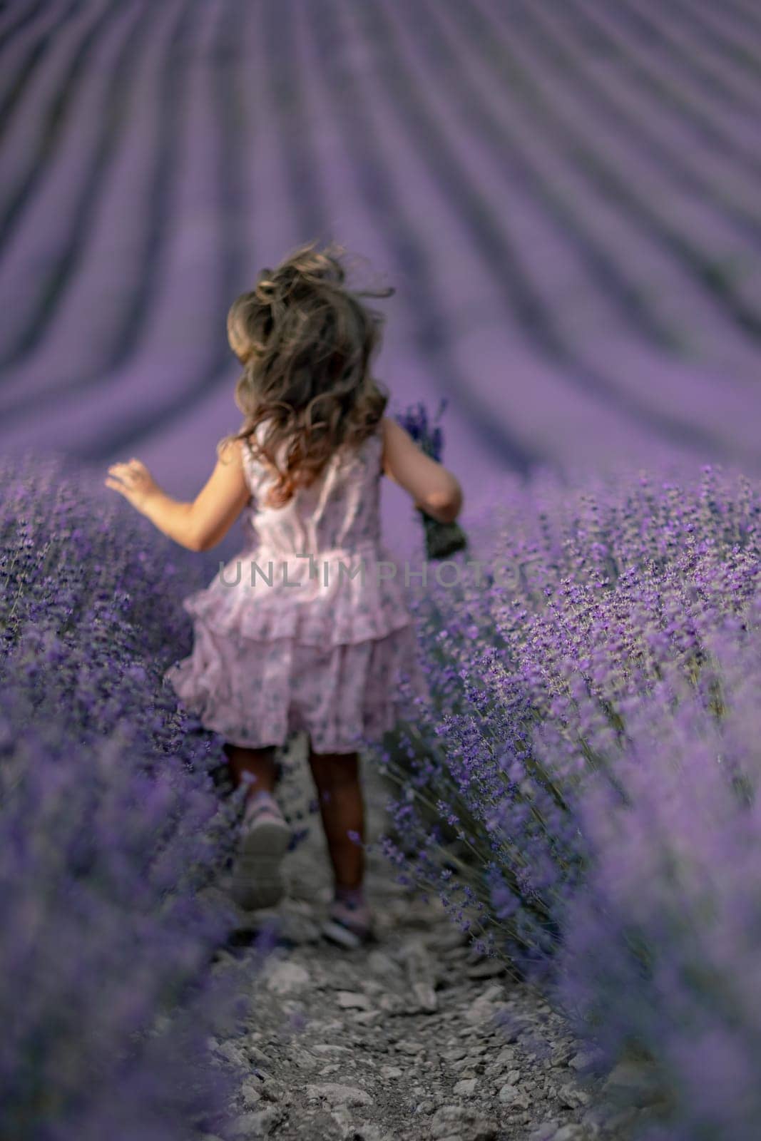 Lavender field girl. Back view happy girl in pink dress with flowing hair runs through a lilac field of lavender. Aromatherapy travel.