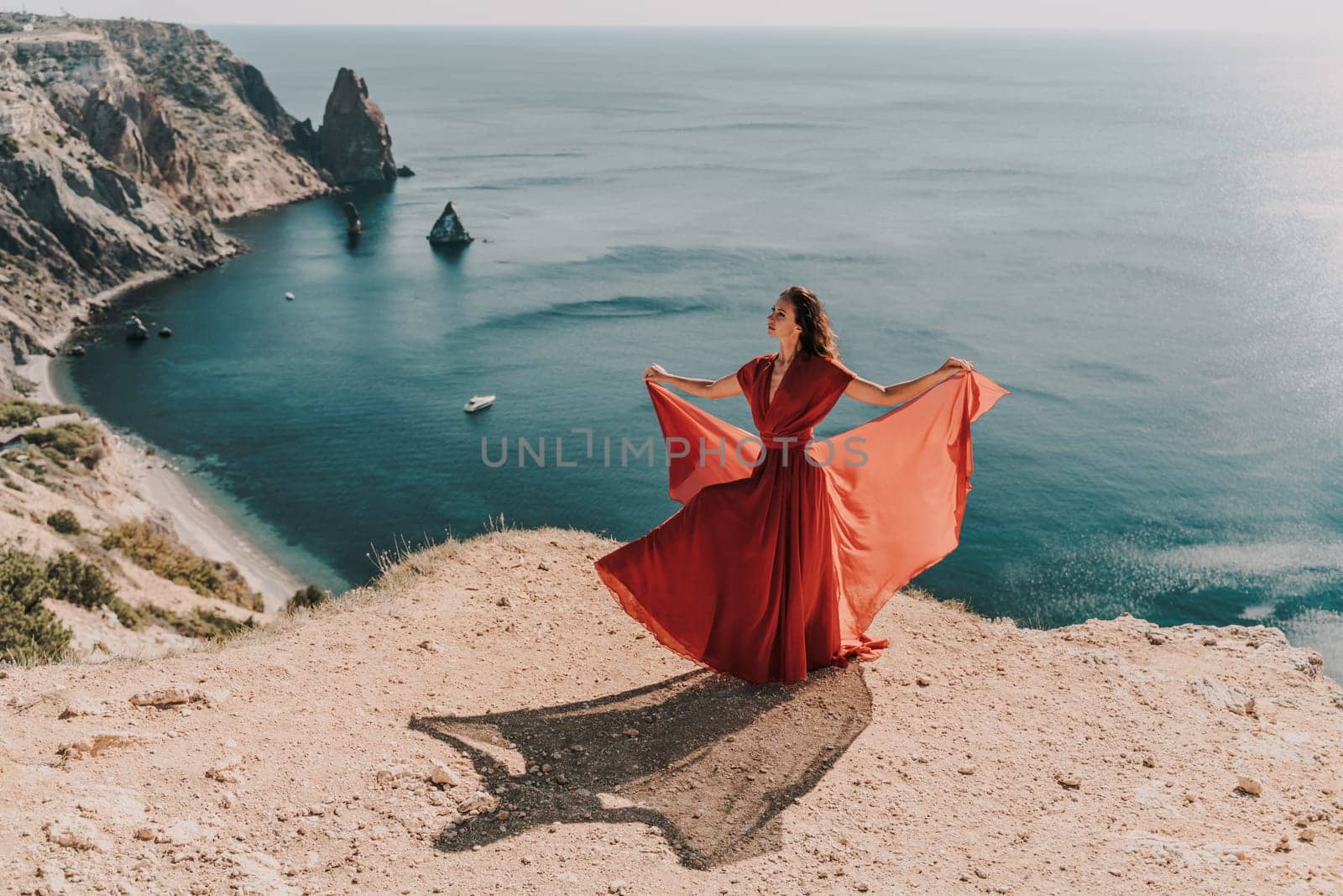 Woman red dress sea., posing on a rocky outcrop high above the sea. Girl on the nature on blue sky background. Fashion photo