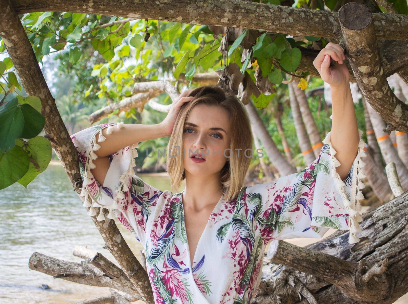 Beautiful young woman standing near palm leaves at sea