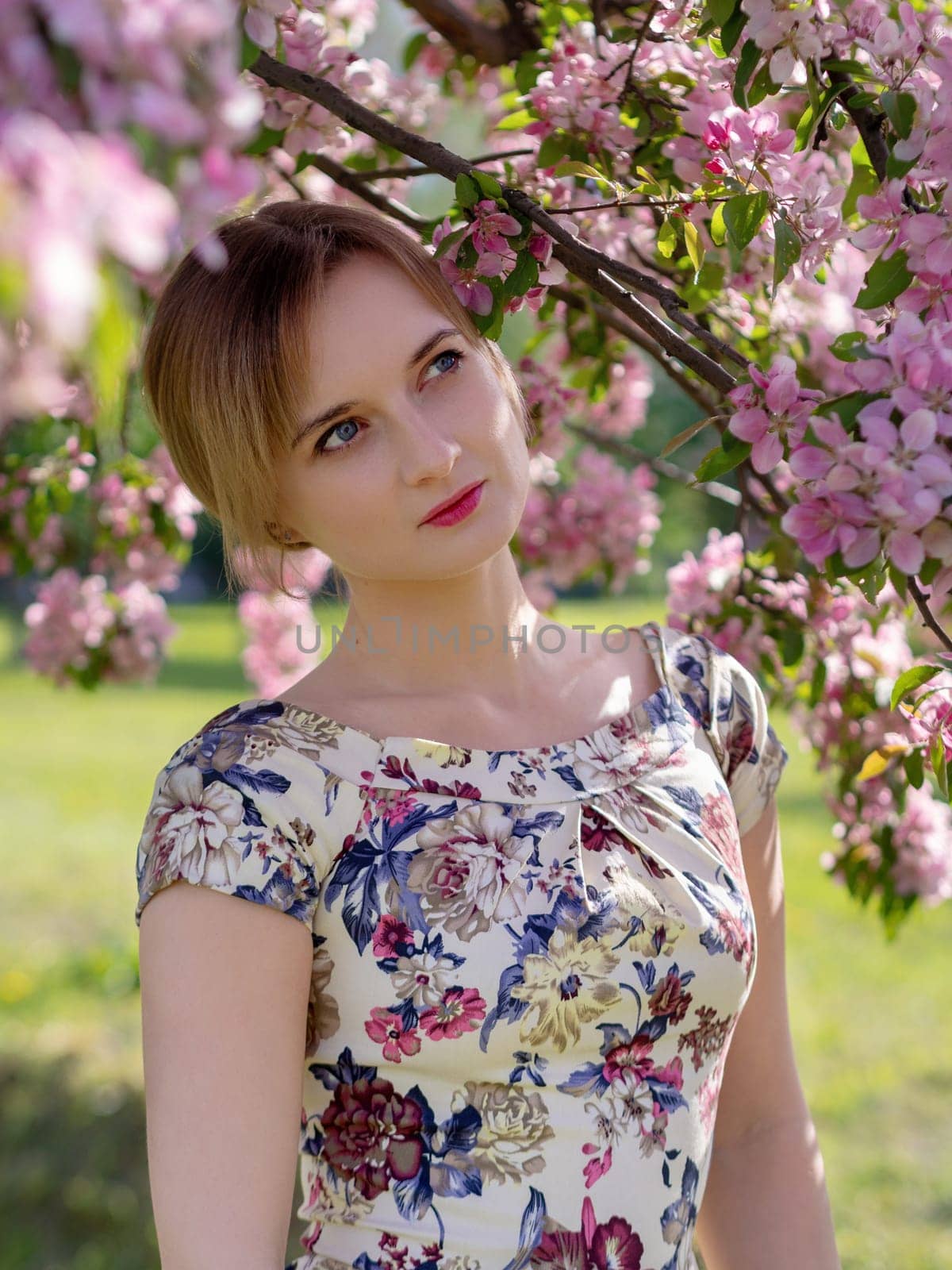 Beautiful young girl in a flowered garden. Tender woman in a dress with a floral print among blooming spring apple trees. by Andre1ns
