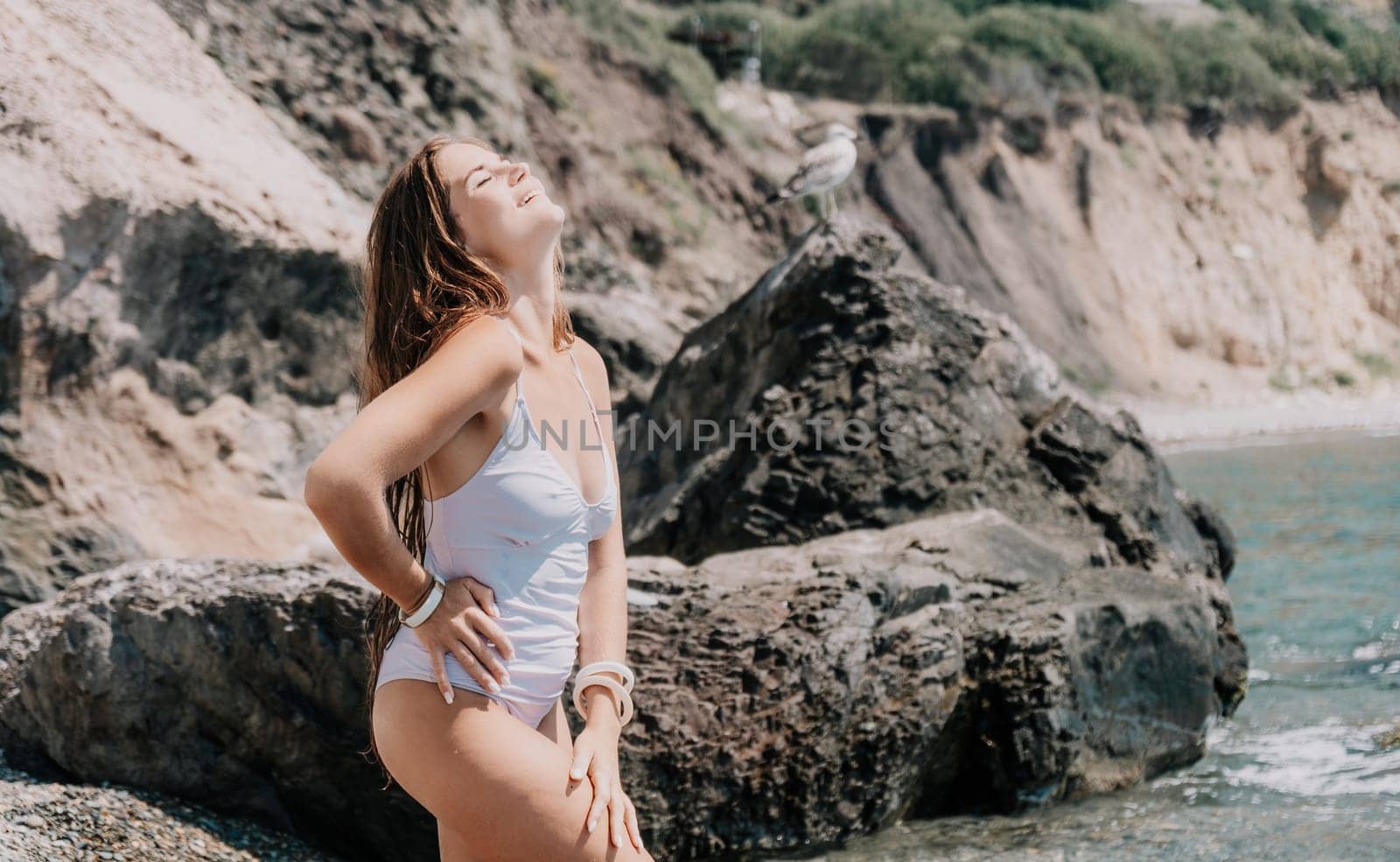 Woman travel sea. Happy tourist in white bikini enjoy taking picture outdoors for memories. Woman traveler posing on the beach at sea surrounded by volcanic mountains, sharing travel adventure journey by panophotograph