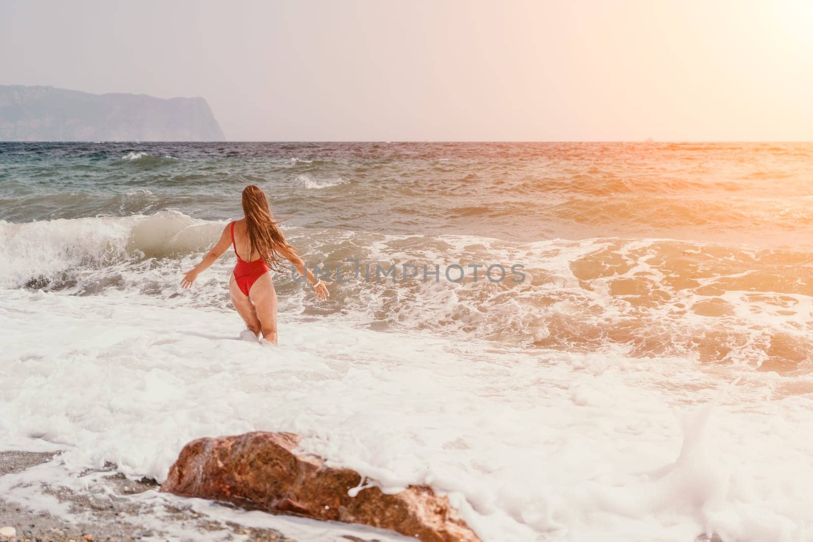 Woman summer travel sea. Happy tourist in red bikini enjoy taking picture outdoors for memories. Woman traveler posing on beach at sea surrounded by volcanic mountains, sharing travel adventure joy by panophotograph