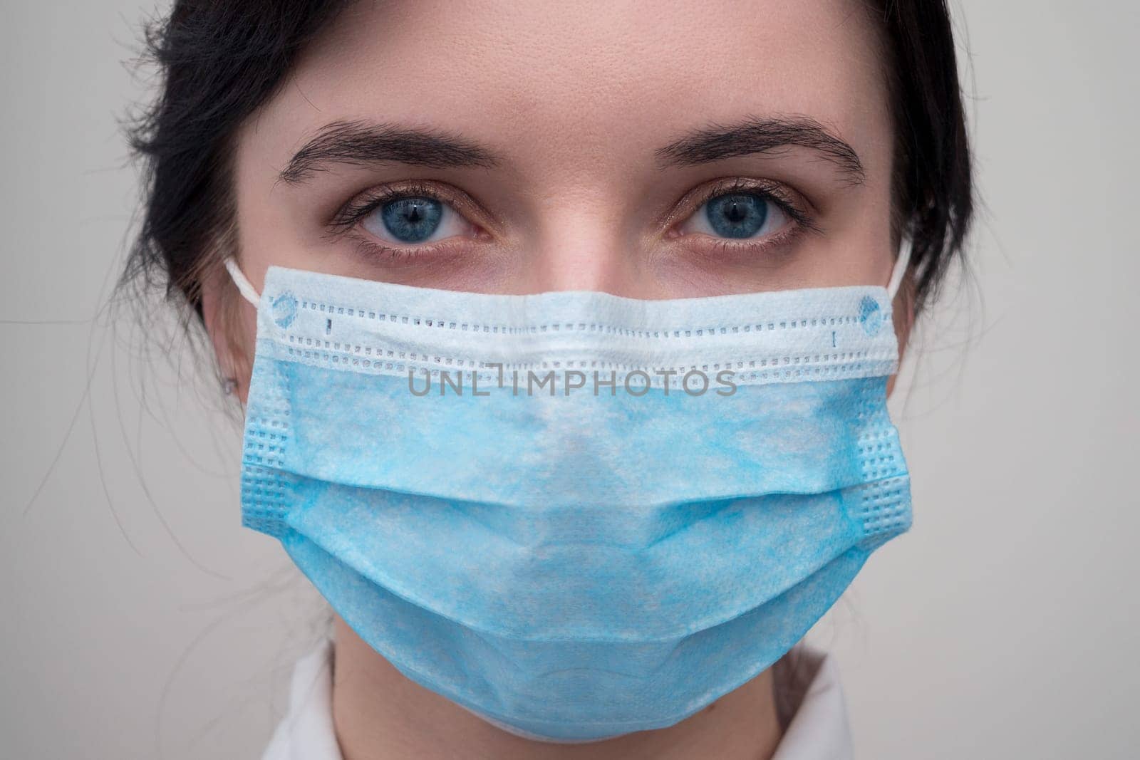 Portrait of a young European woman in a protective disposable medical mask. Concept of caronavirus Cavid 19 and human quarantine. Girl in a mask on a white wall. Masked medical worker. by Andre1ns