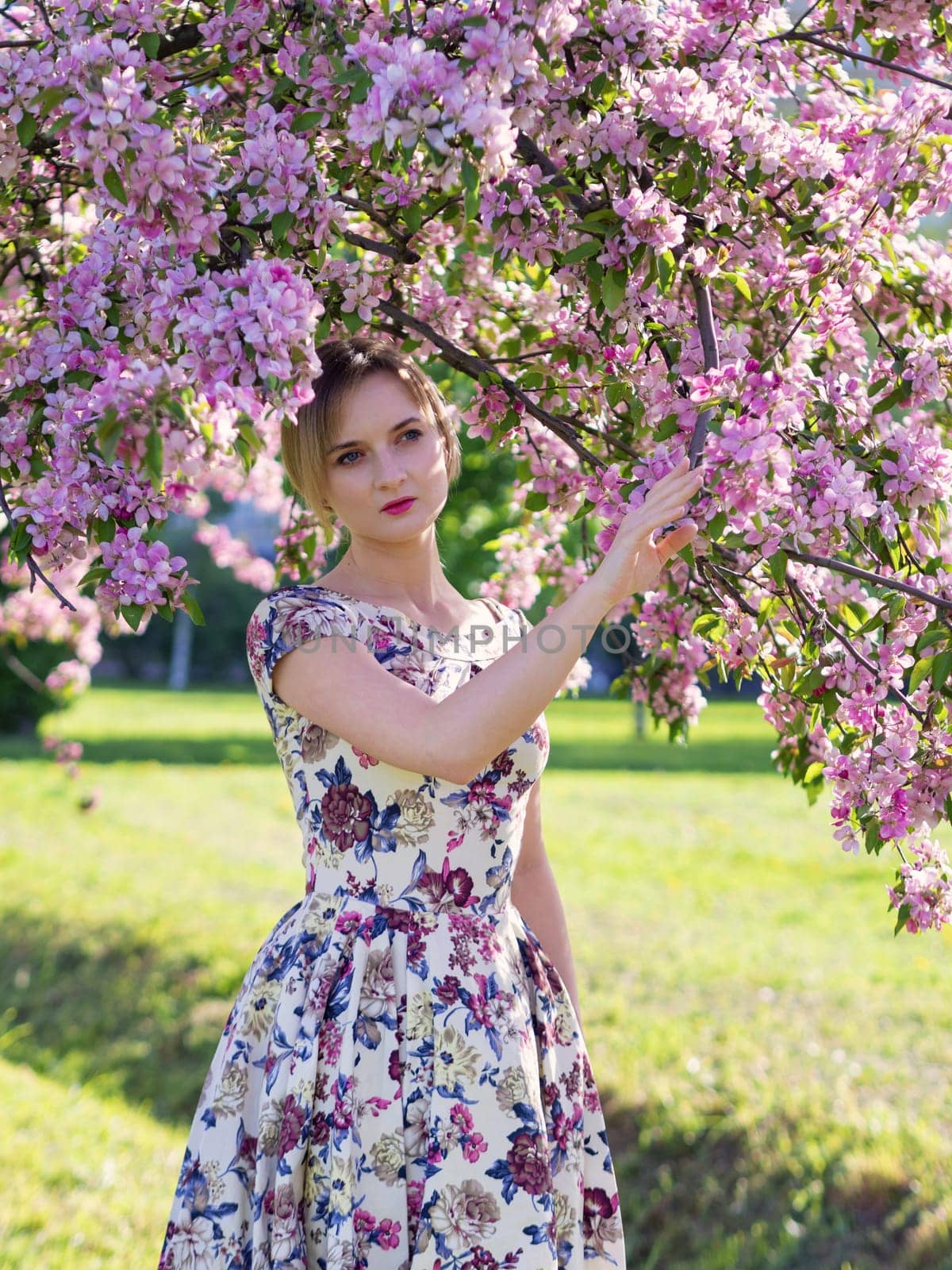 Beautiful young girl in a flowered garden. Tender woman in a dress with a floral print among blooming spring apple trees. by Andre1ns