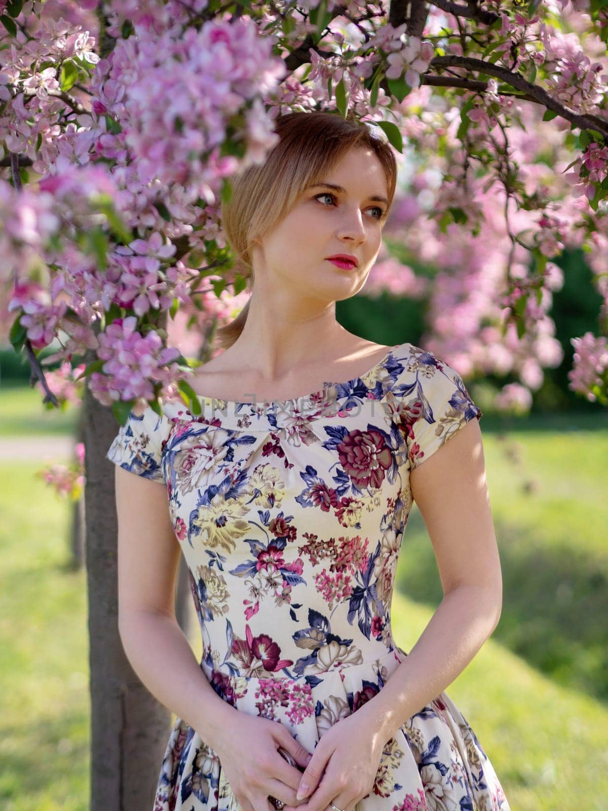 Beautiful young girl in a flowered garden. Tender woman in a dress with a floral print among blooming spring apple trees. by Andre1ns