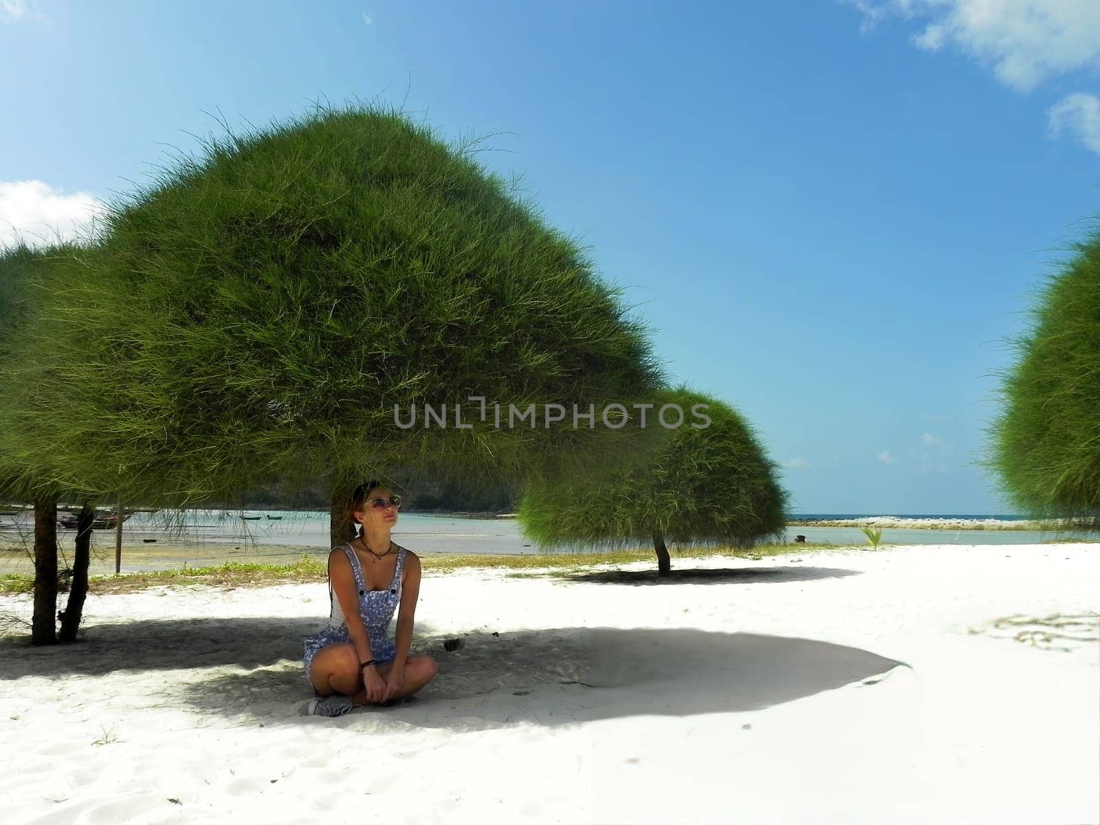 Young woman sit on the sand on a tropical sandy beach in the shade of trees. Malibu Beach, Koh Phangan, Thailand.
