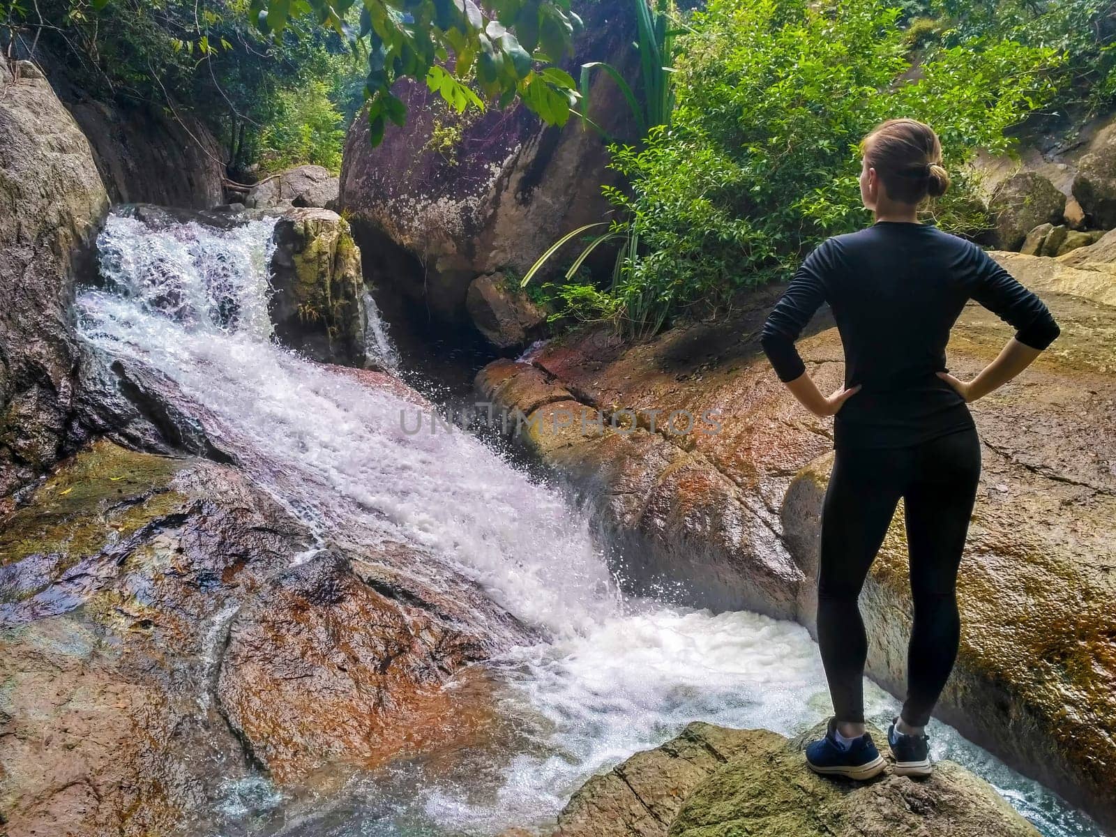 A girl in a black tracksuit looks at a waterfall in the jungle. Tracking.