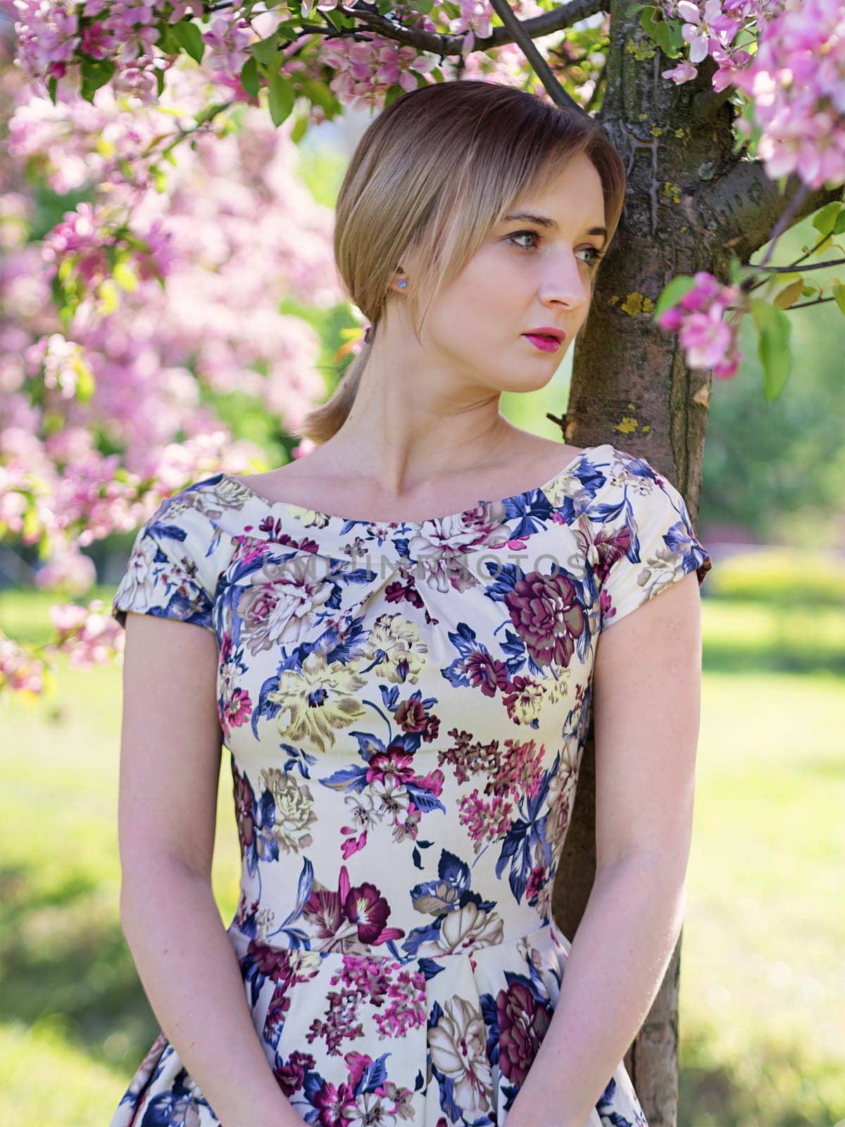 Beautiful young girl in a flowered garden. Tender woman in a dress with a floral print among blooming spring apple trees. by Andre1ns