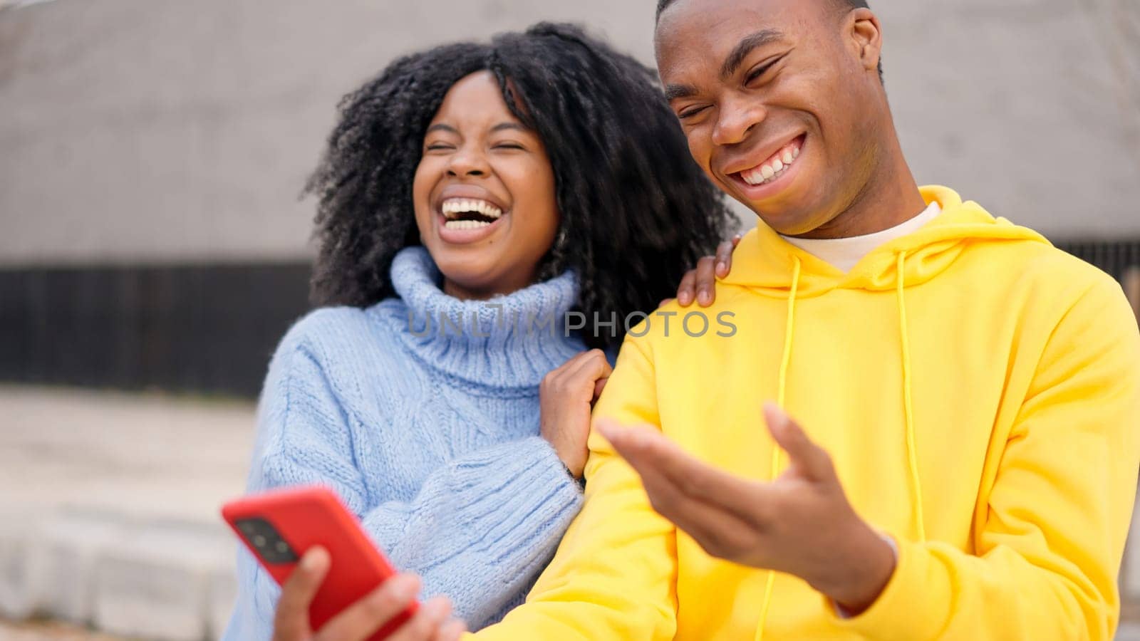 Young african couple having fun using mobile in the street