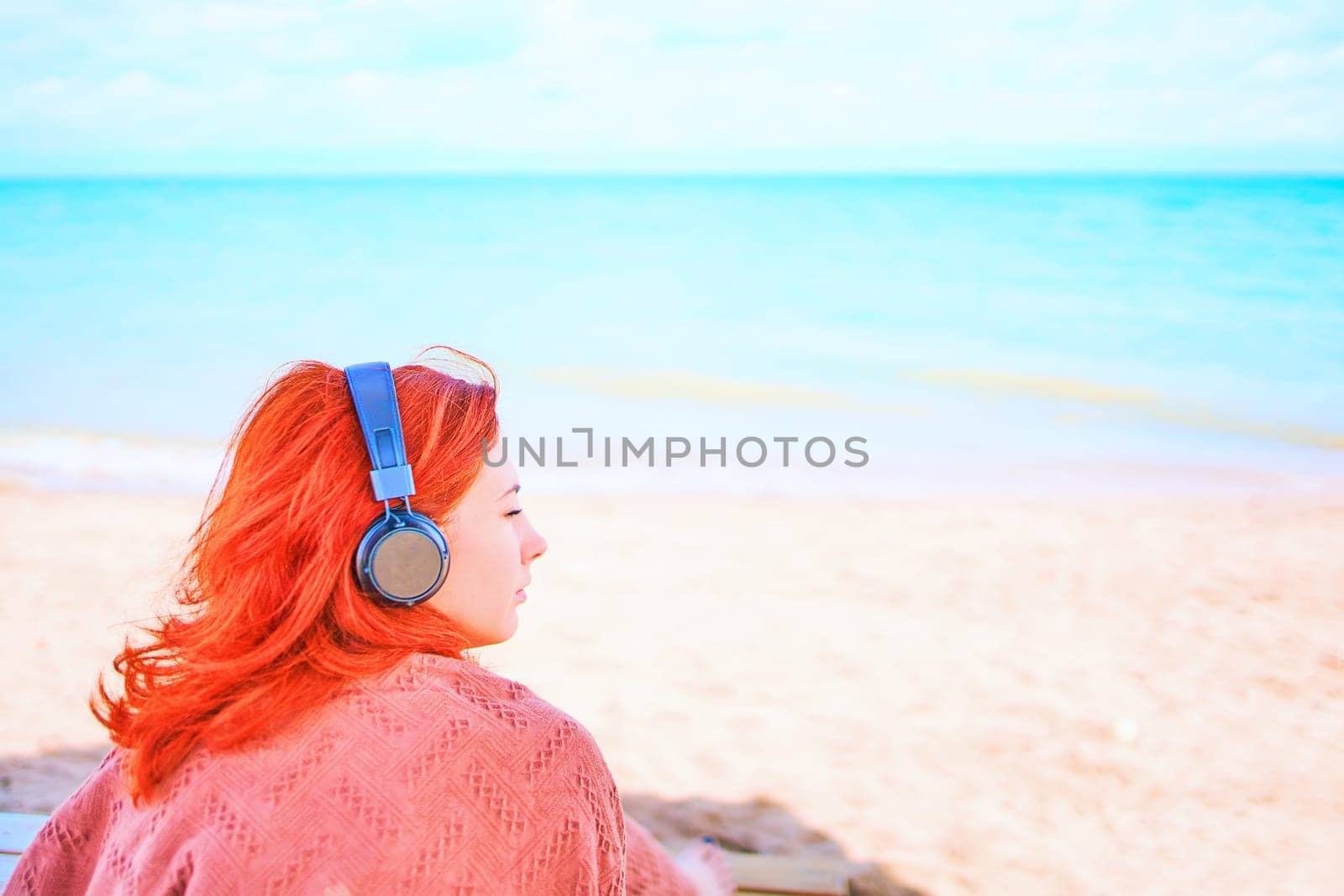 Cute redhead woman with headphones listening to music on the beach.