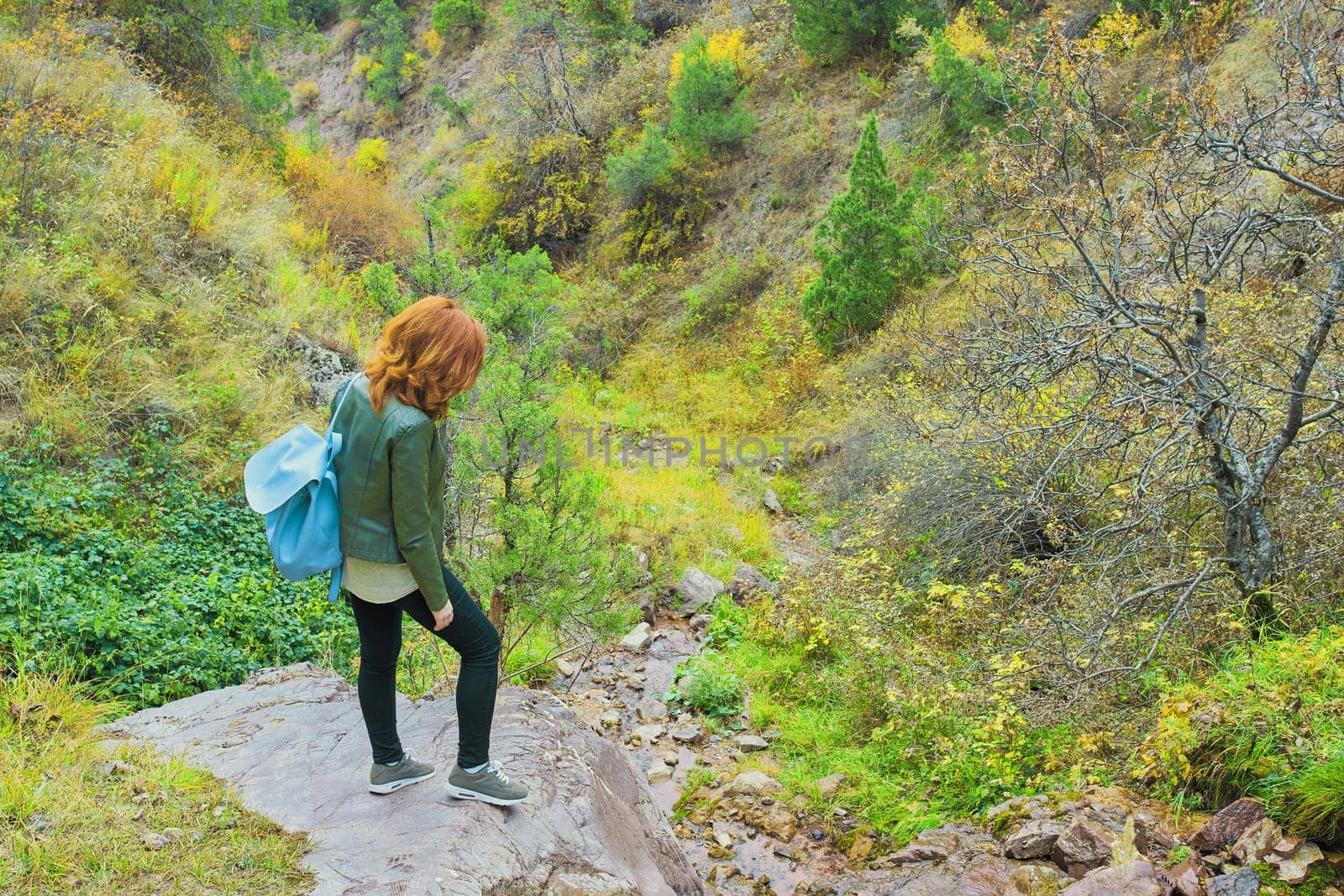 Female hiker walking in mountains forest. Woman tourist with a backpack admires the mountain rock.