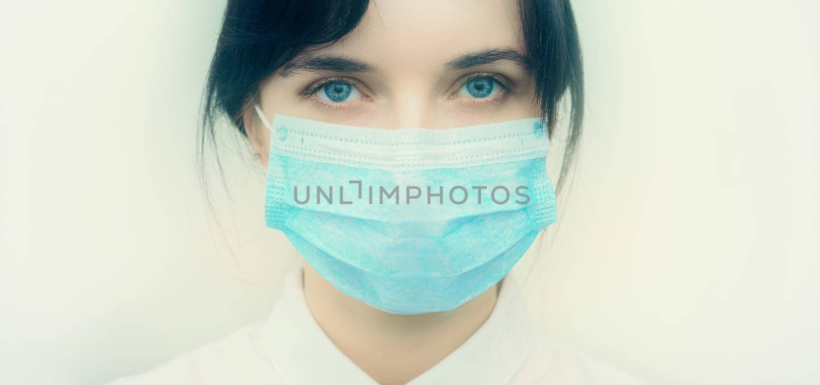 Portrait of a young European woman in a protective disposable medical mask. Concept of caronavirus Cavid 19 and human quarantine. Girl in a mask on a white wall. Masked medical worker. by Andre1ns