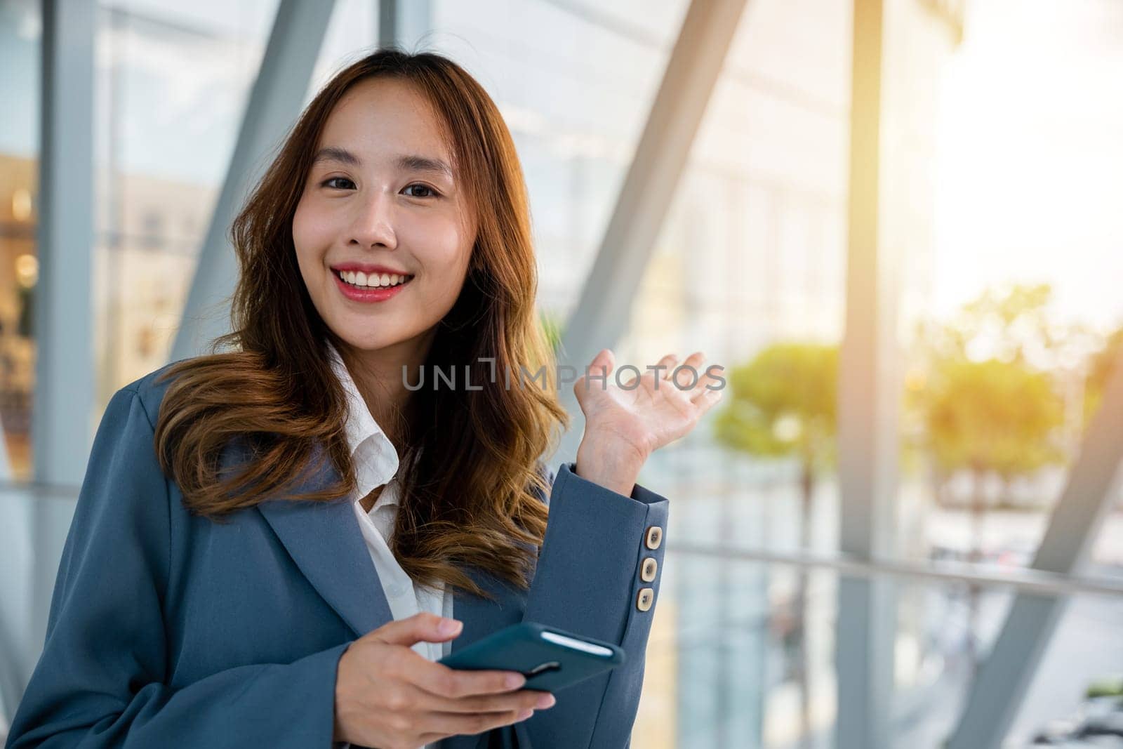 Smiling young woman using her smartphone for messaging, browsing and calling on a bright and modern urban background.
