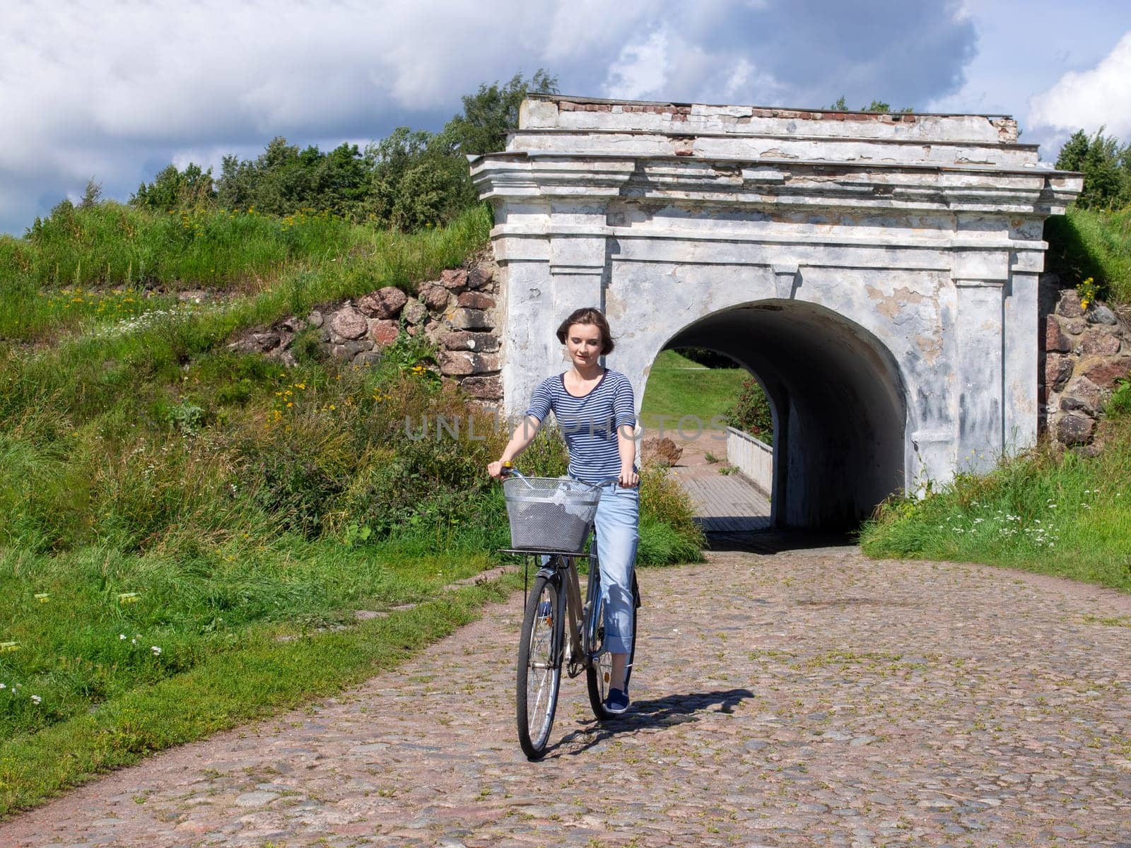 A woman is riding a blue bicycle with a basket of paving stones.
