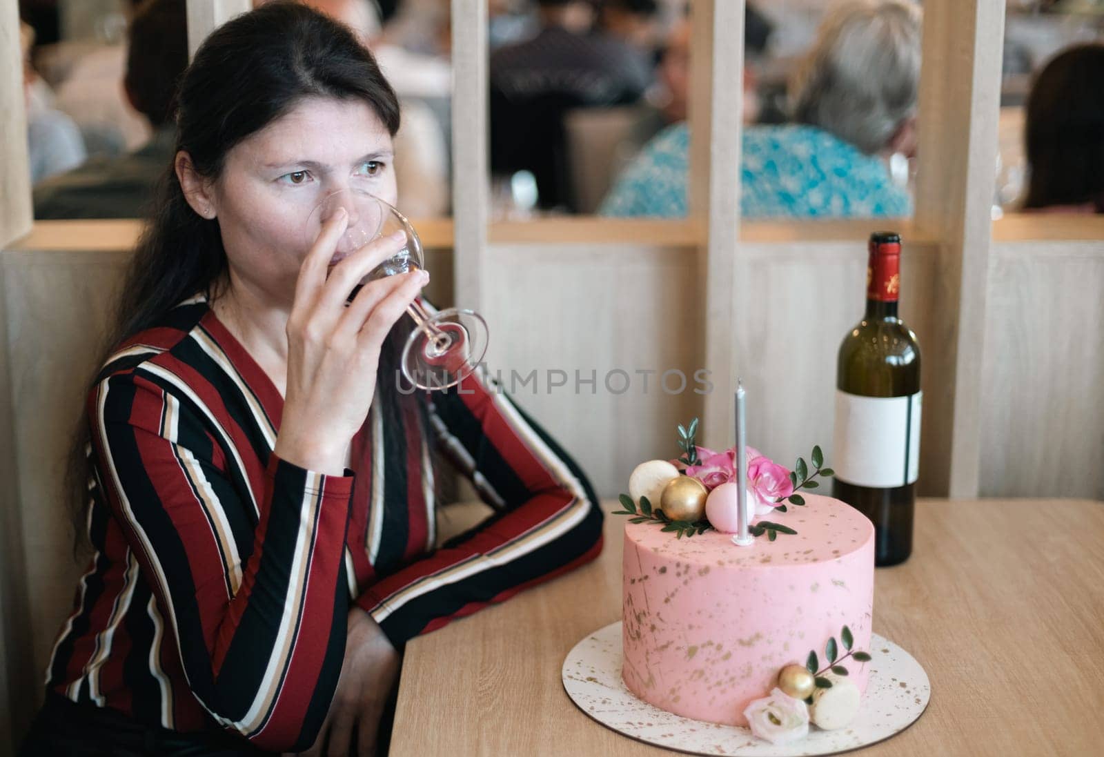 A girl drinks wine from a glass while sitting at a table with a cake. by Nataliya