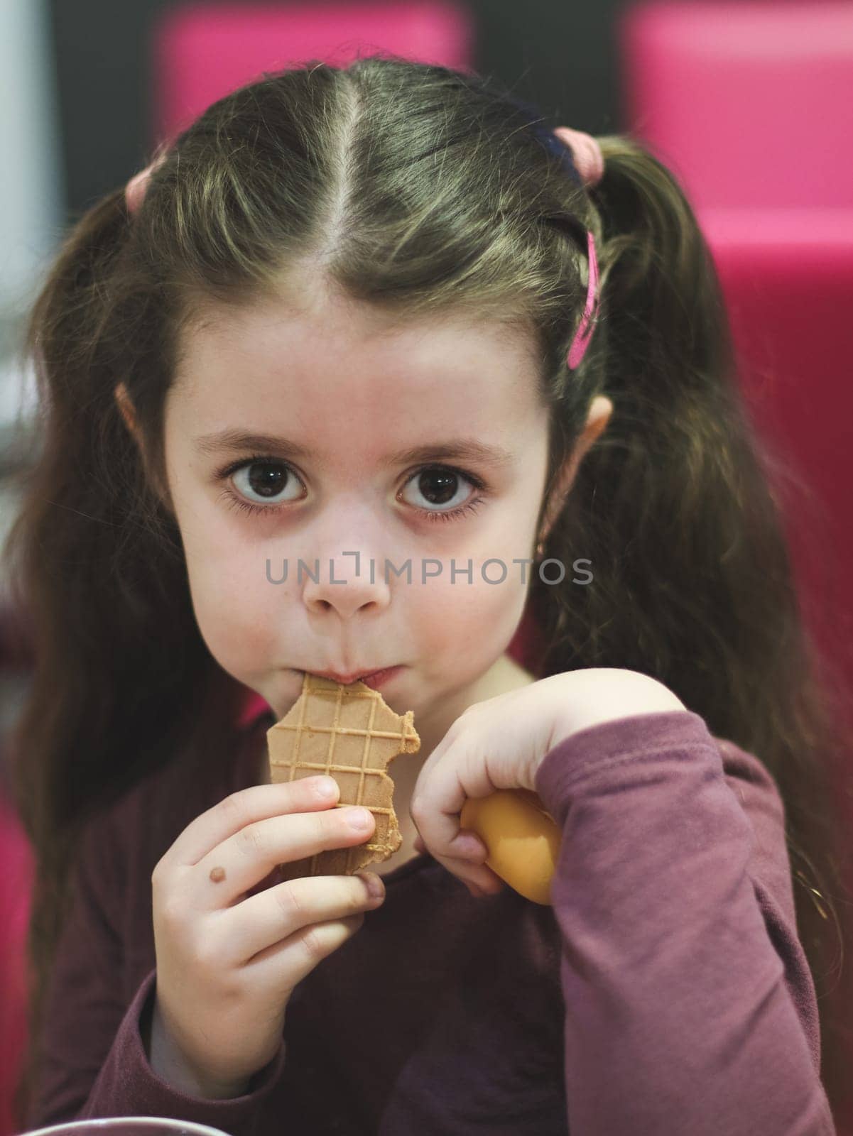 Portrait of a beautiful Caucasian brunette girl with big brown eyes sitting at a table and eating an ice cream waffle in a cafe on a blurred background, close-up side view with depth of field.