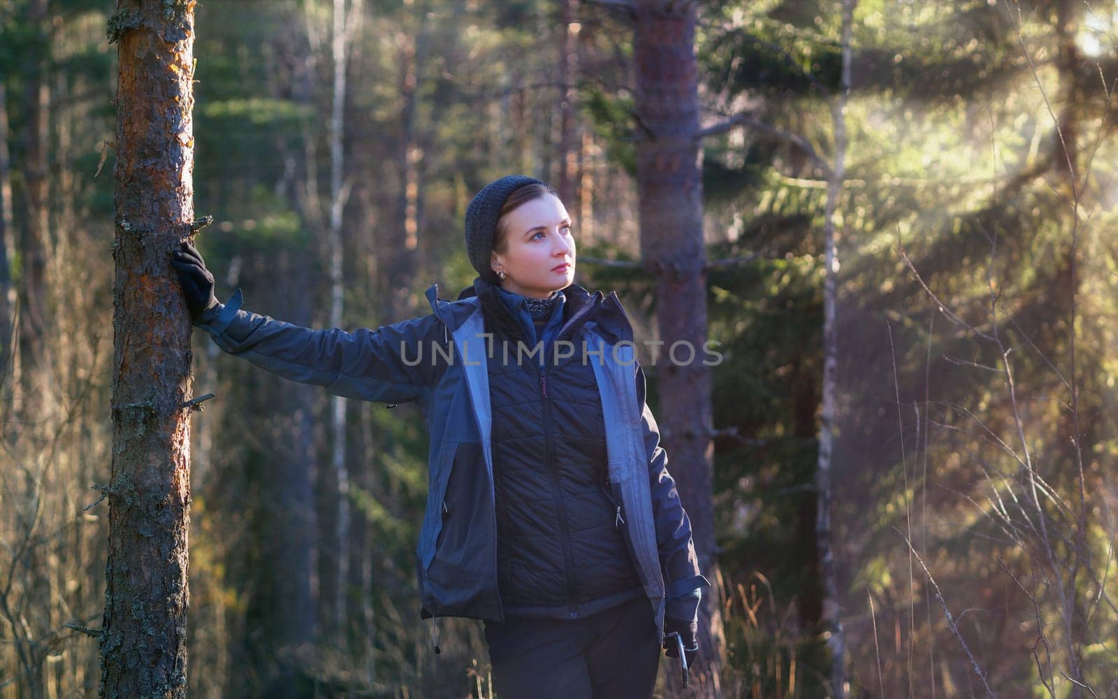 Happy woman hiker leaned against a tree in a sunny forest by Andre1ns