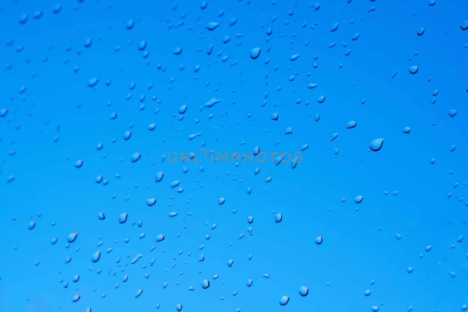 Raindrops on the surface of window glass with a blurred background.