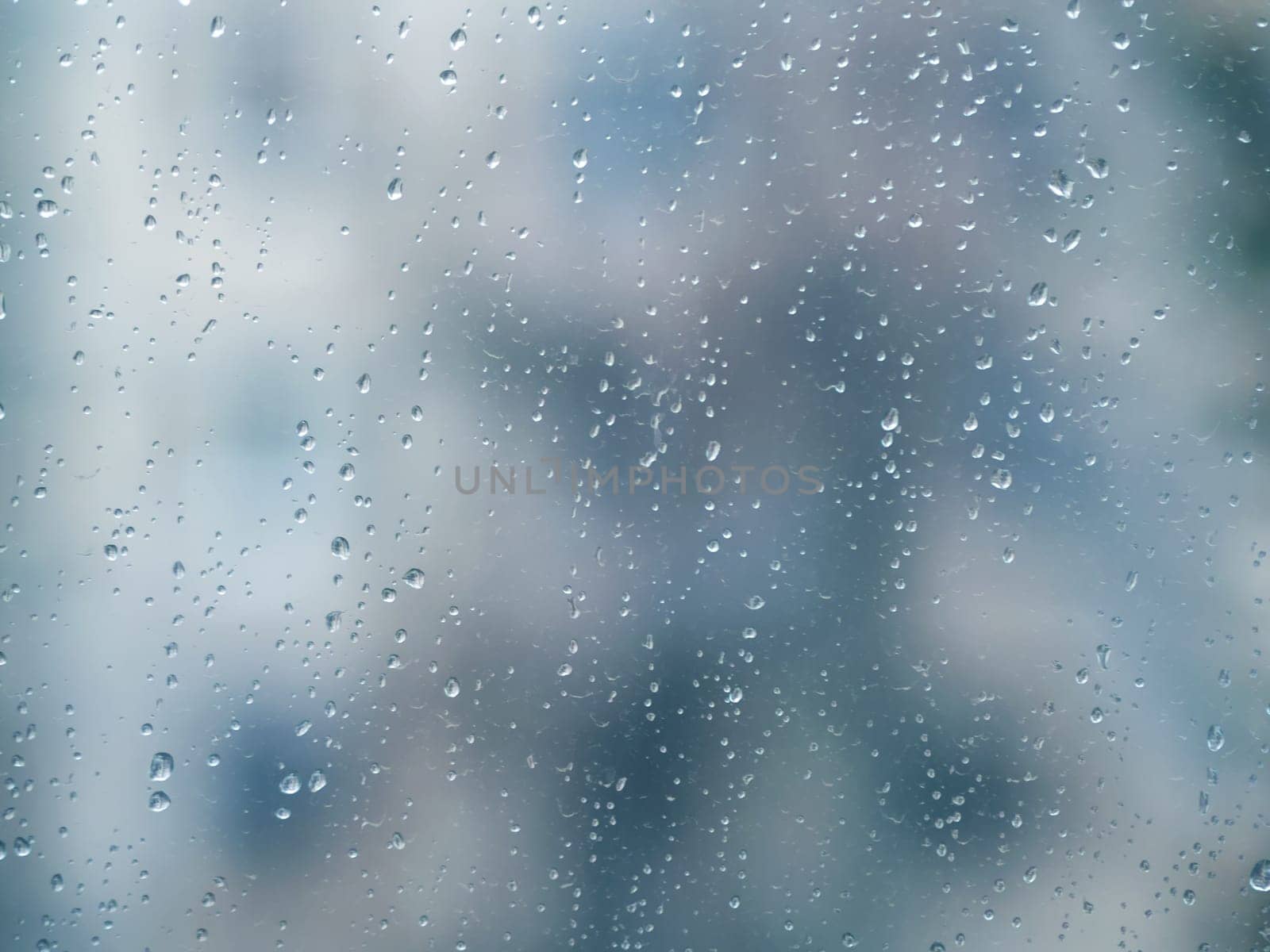 Raindrops on the surface of window glass with a blurred background.