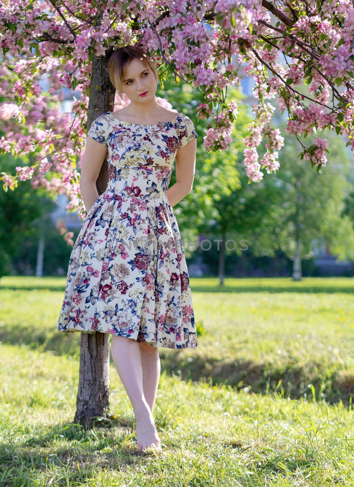 Beautiful young girl in a flowered garden. Tender woman in a dress with a floral print among blooming spring apple trees. by Andre1ns